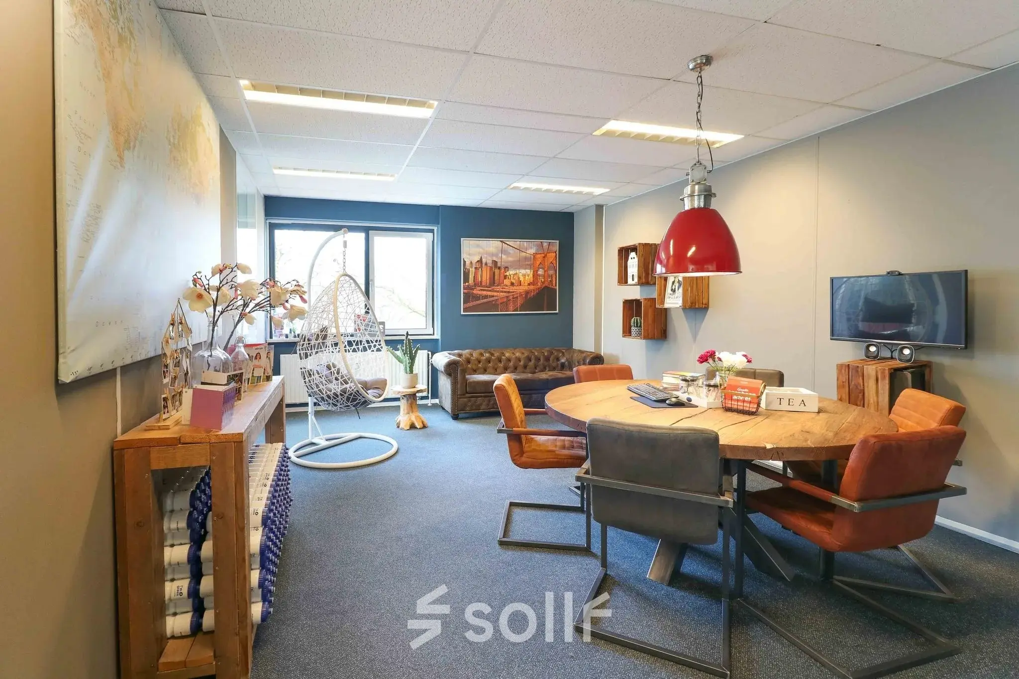 Cozy office space for rent in Apeldoorn with a mix of modern and vintage furniture, featuring a round table, chairs, and a comfortable seating area.