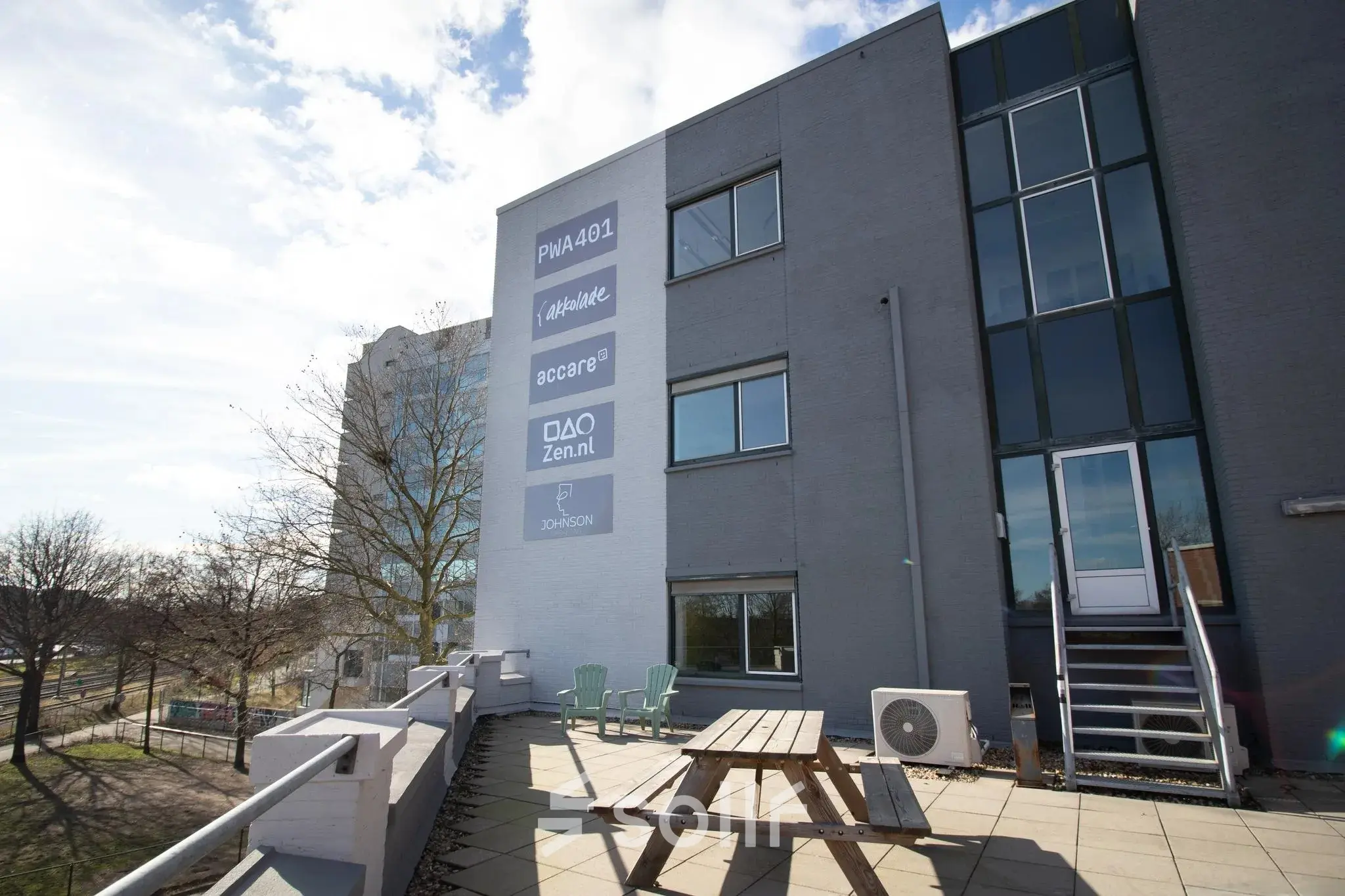 Exterior view of the office building at Prins Willem-Alexanderlaan 401 in Apeldoorn with a terrace featuring a picnic table and outdoor chairs. Ideal for rent office space seekers.
