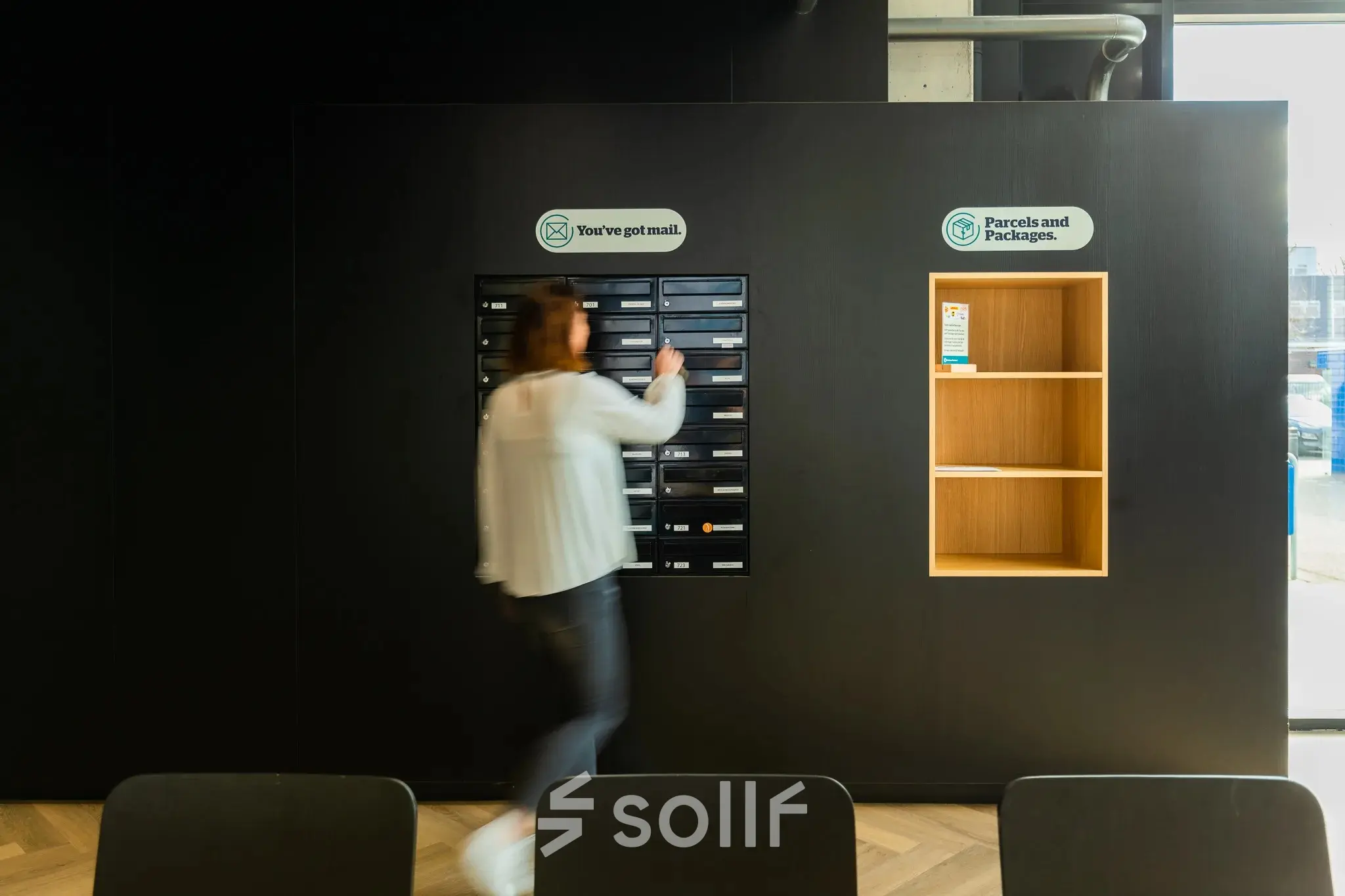 Person in an office lobby area managing mailboxes along a sleek, modern wall designed for office space rental at Prins Willem Alexanderlaan 701, Apeldoorn.