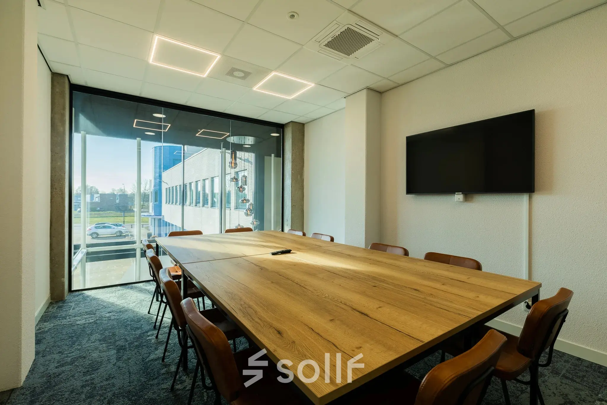Modern conference room available for office space rental at Prins Willem Alexanderlaan 701, Apeldoorn, featuring a large wooden table, chairs, a wall-mounted screen, and a bright window view.