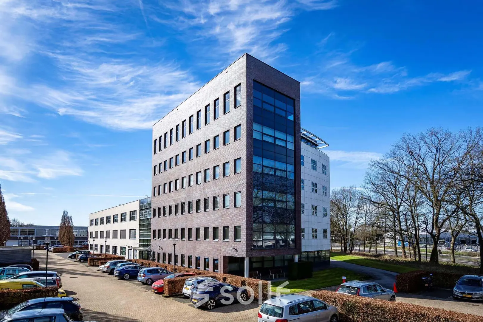 Exterior view of an office building at Schumanpark 9, Apeldoorn, suitable for office space rental, with ample parking space visible.