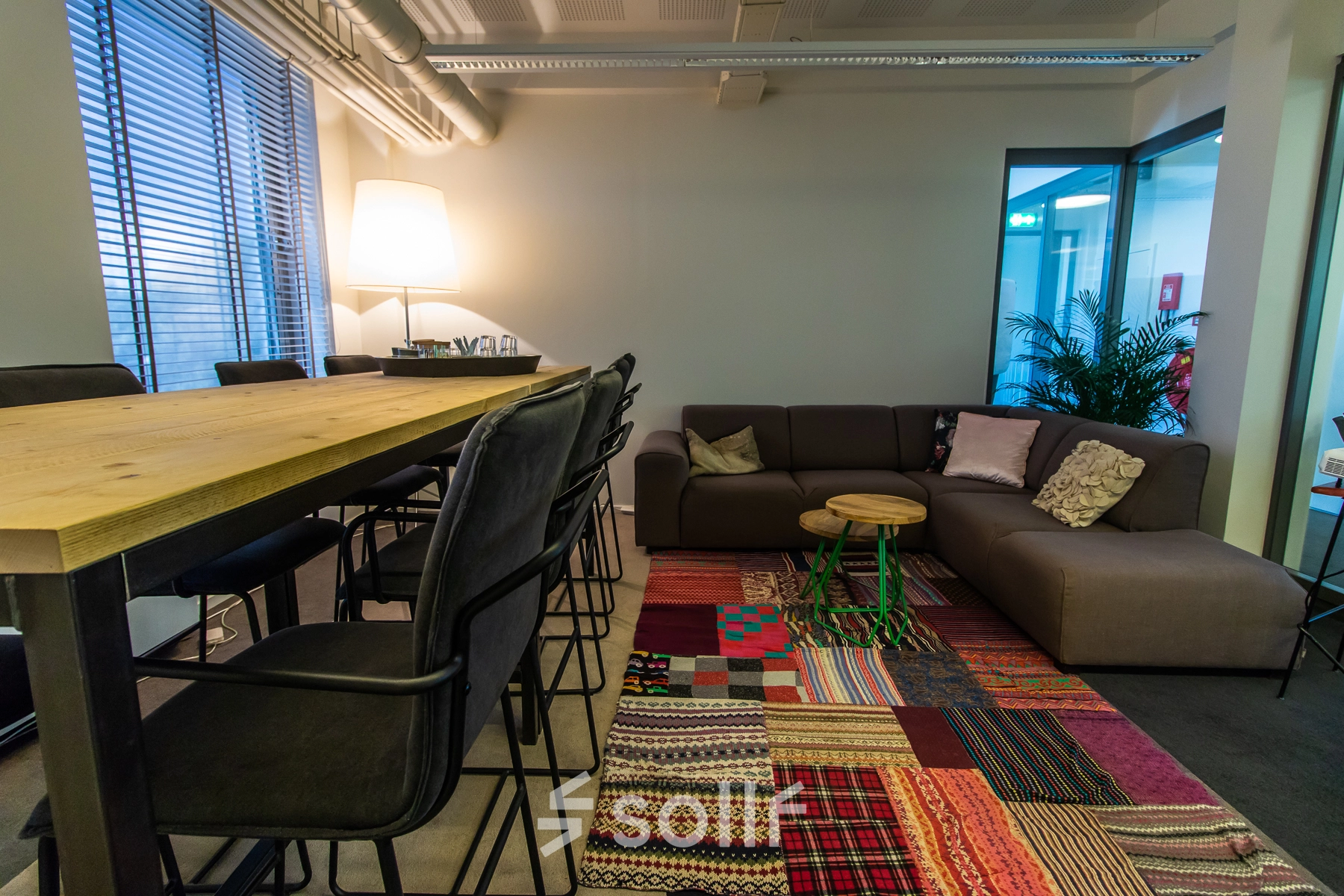 Cozy and vibrant office space at Jansbuitensingel 7, Arnhem Centrum, perfect for rent with a mix of seating options, colorful rug, and warm lighting.