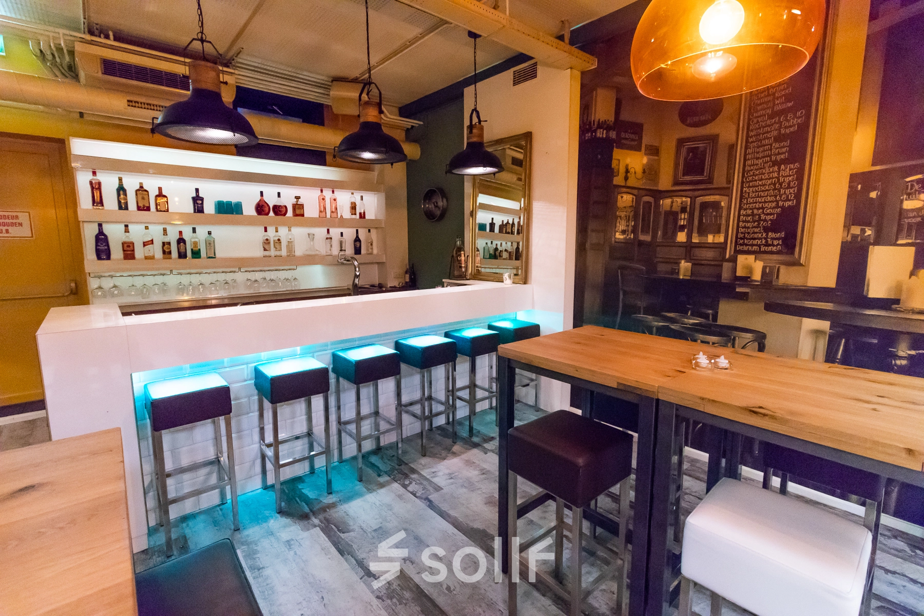 A modern office lounge in Arnhem Centrum at Jansbuitensingel 7, featuring a stylish bar setup with high stools and ambient lighting, ideal for rent office space activities.