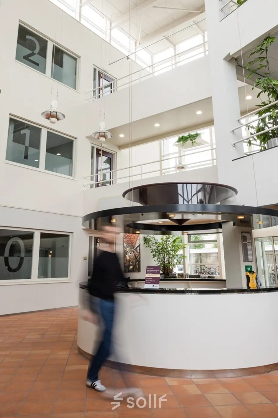 Modern office to rent at Vlamoven 34, Arnhem IJsseloord, featuring an open atrium with individuals walking through the reception area.