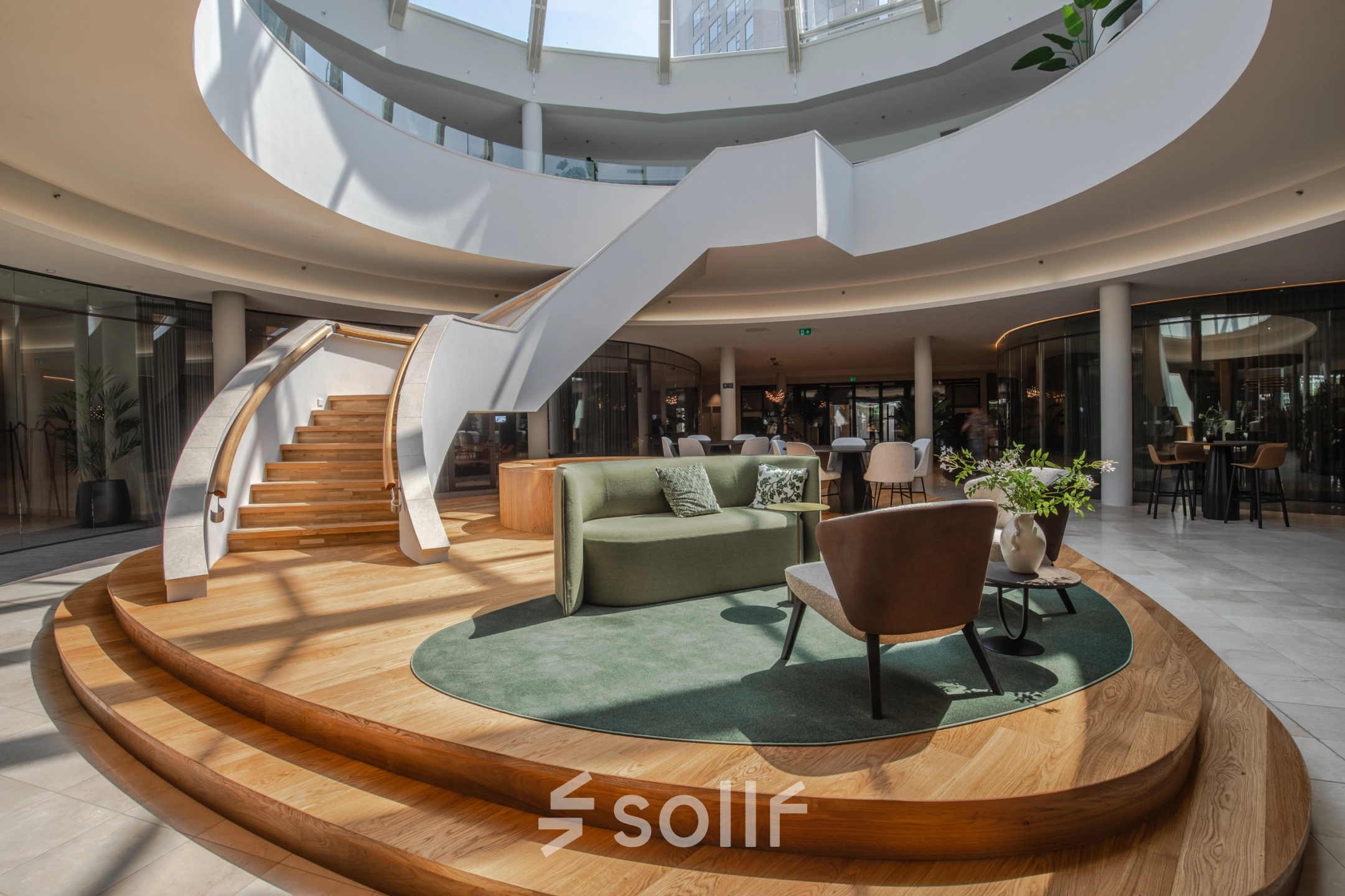 A modern office space for rent in Arnhem Zuid, featuring a stylish lounge area with seating surrounded by curved architecture and a spiral staircase under a skylight.