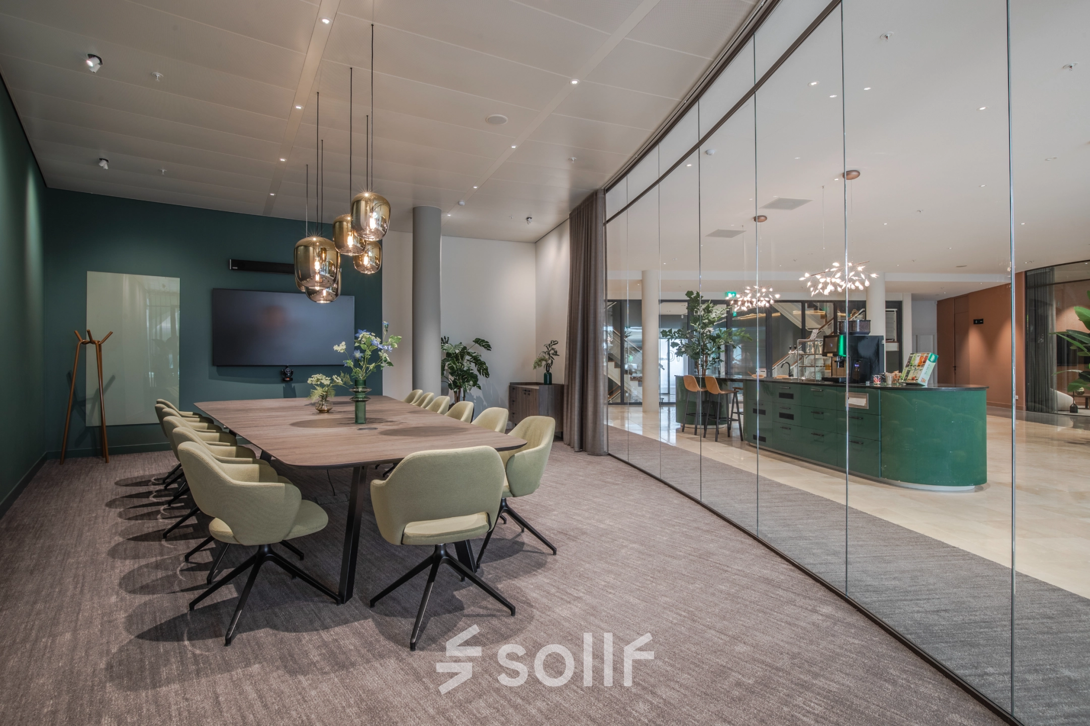 Stylish office space rental in Arnhem Zuid featuring a modern conference room with a long table and green chairs. Adjacent reception area visible through glass wall.