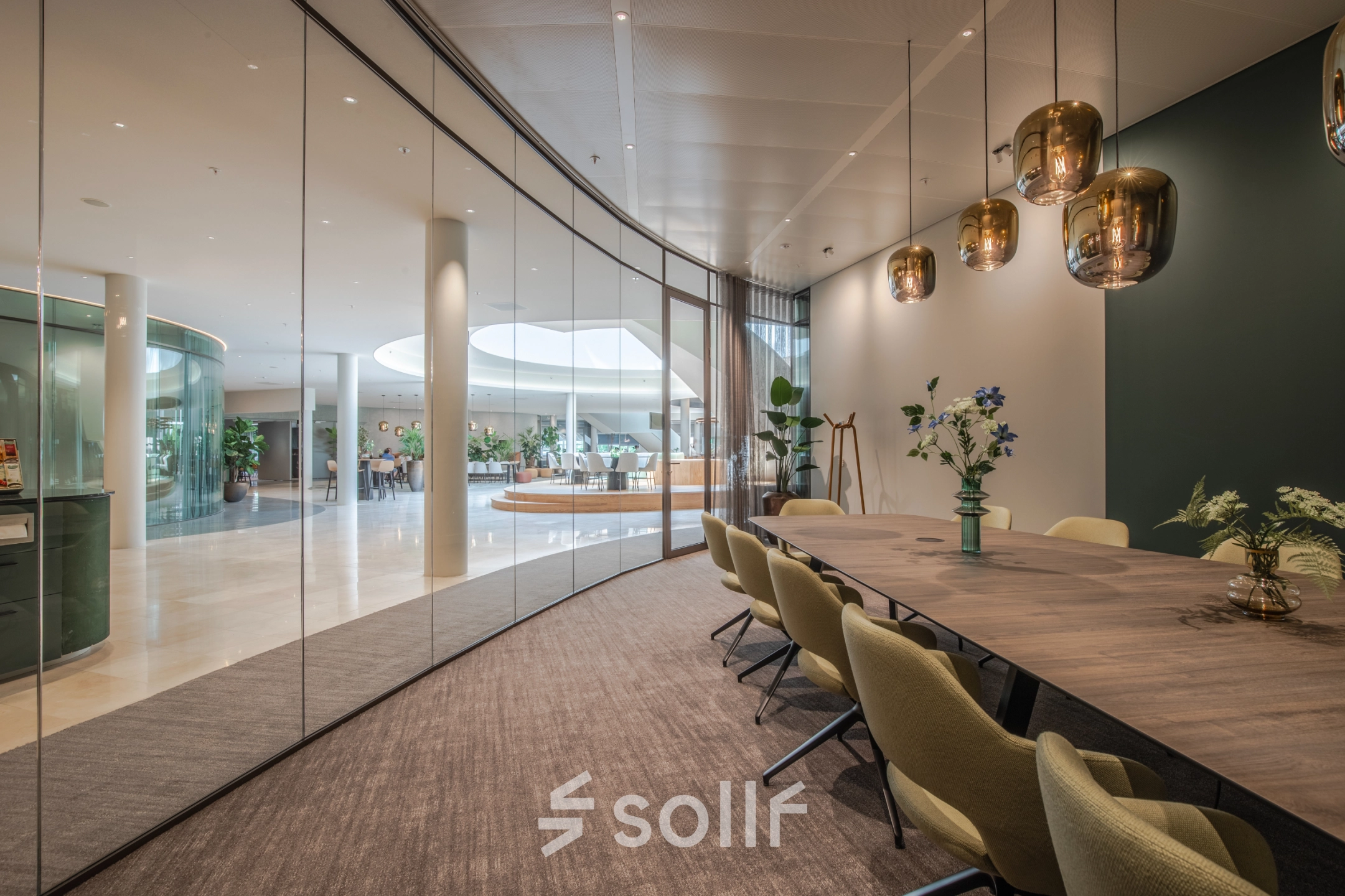 Modern conference room with glass walls, surrounded by a lush, open-floor work area. Ideal for office space rental at Rijksweg-West 2, Arnhem Zuid.