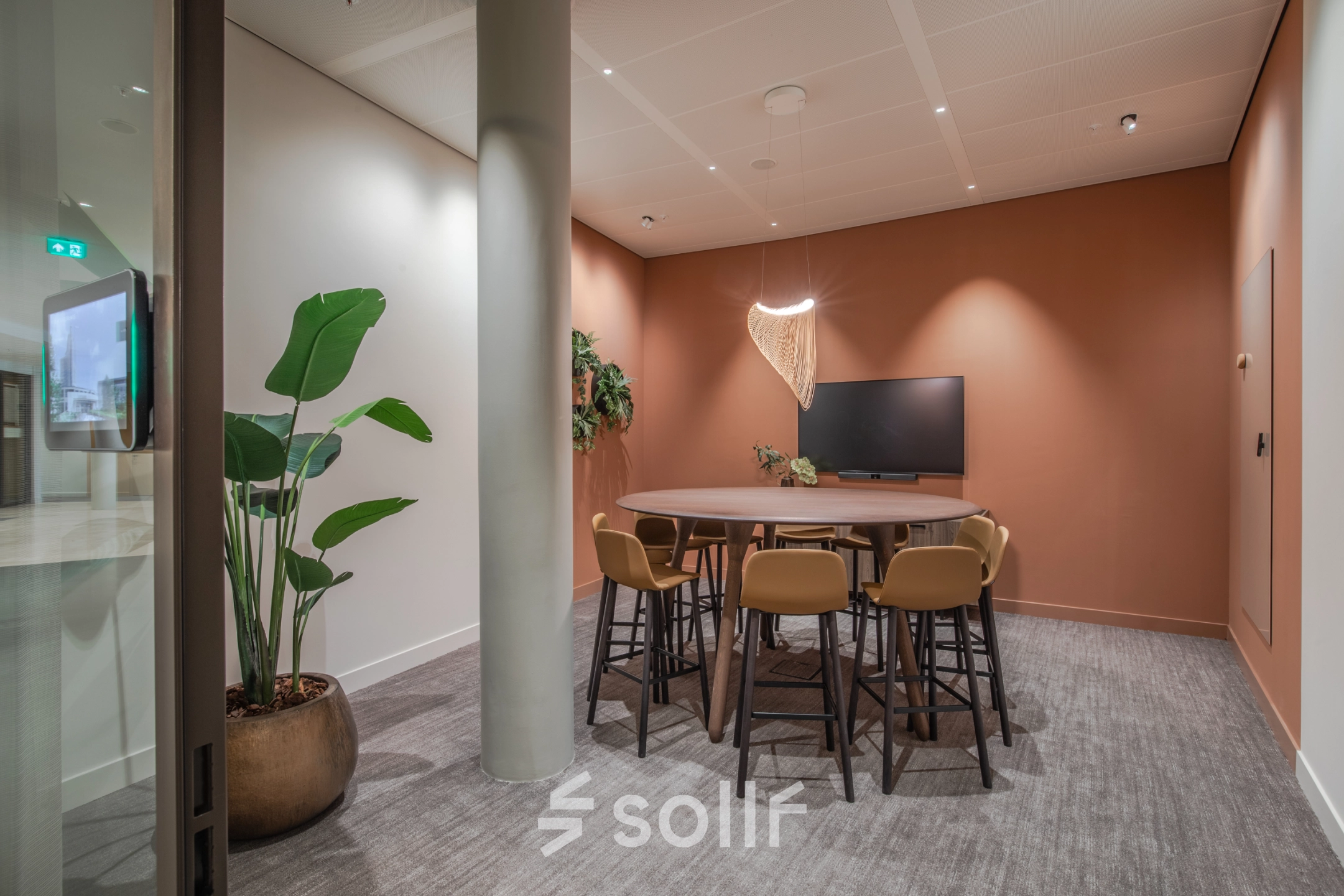Modern conference room at Rijksweg-West 2, Arnhem Zuid, featuring a round table, chairs, a wall-mounted screen, and warm lighting. Ideal for office space rental.