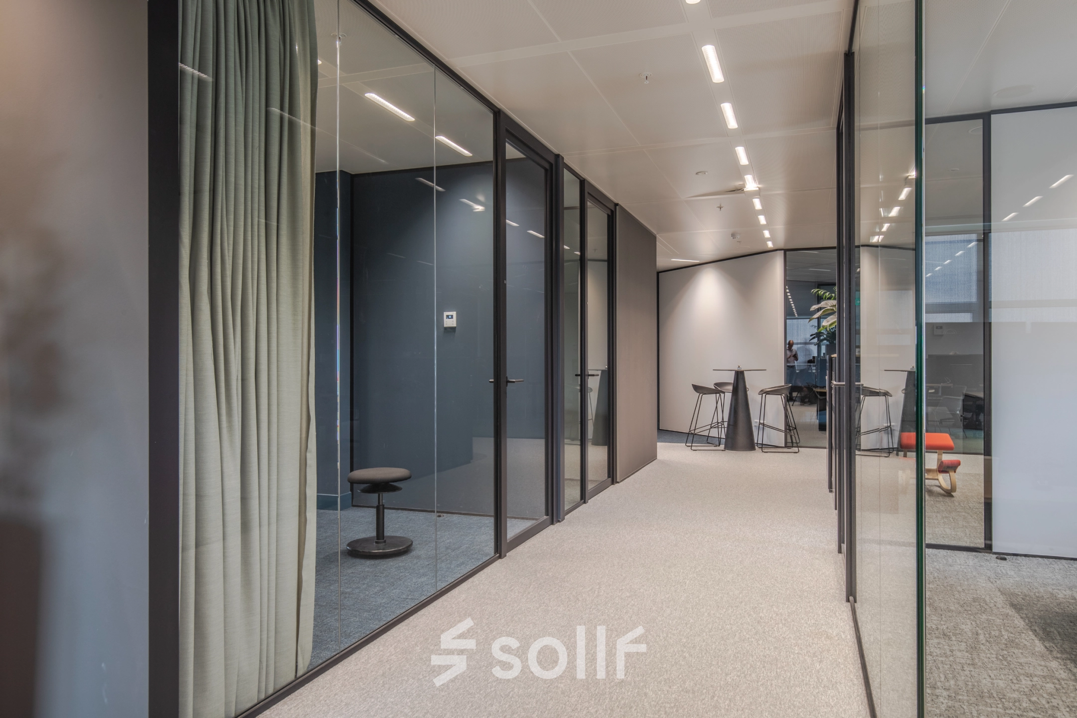 Modern office space for rent in Arnhem Zuid featuring glass-walled rooms with sleek furnishings and high ceilings.