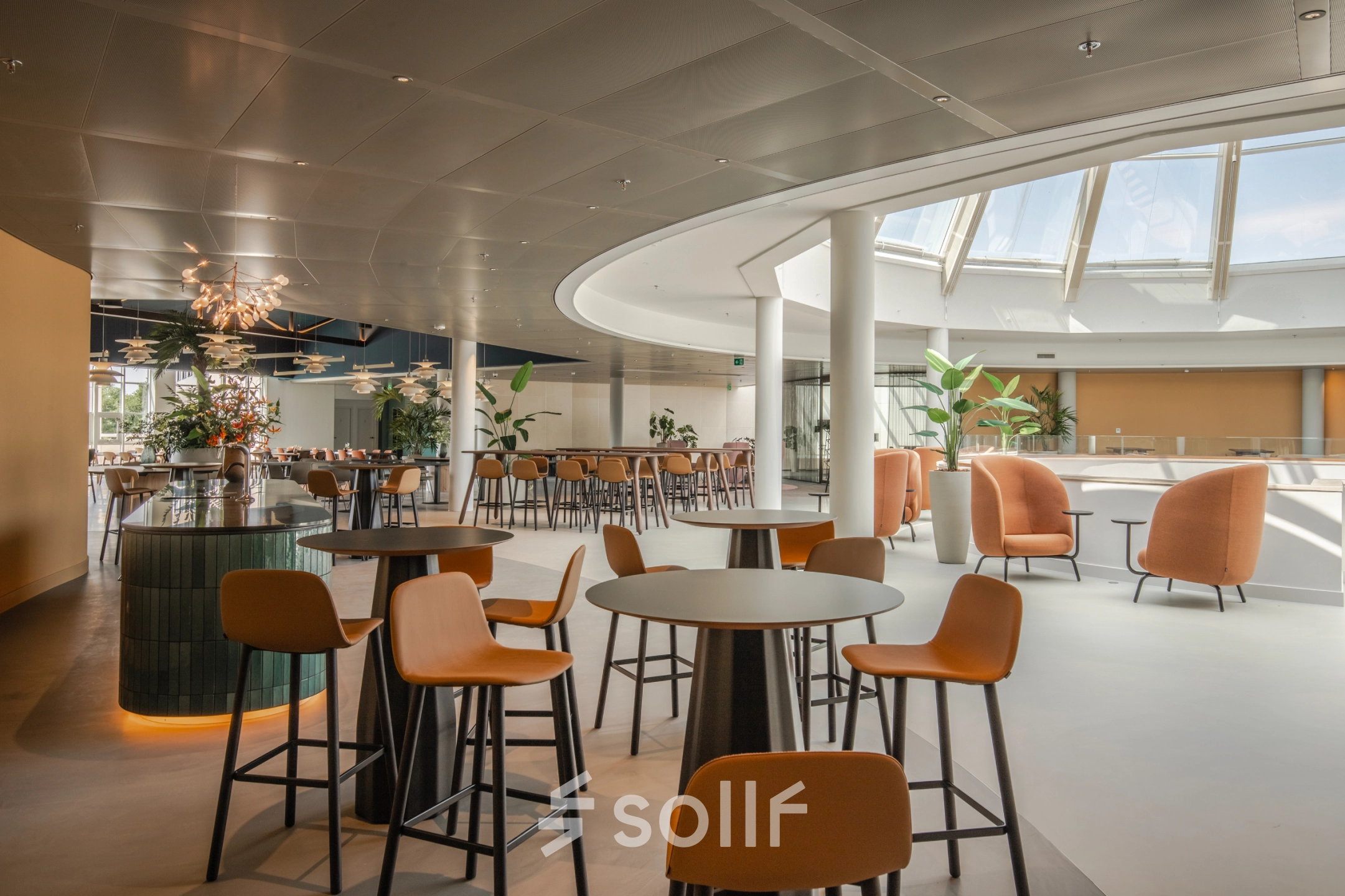 Spacious, modern workspace with round tables and chairs under a skylight, ideal for office space rental in Arnhem Zuid.