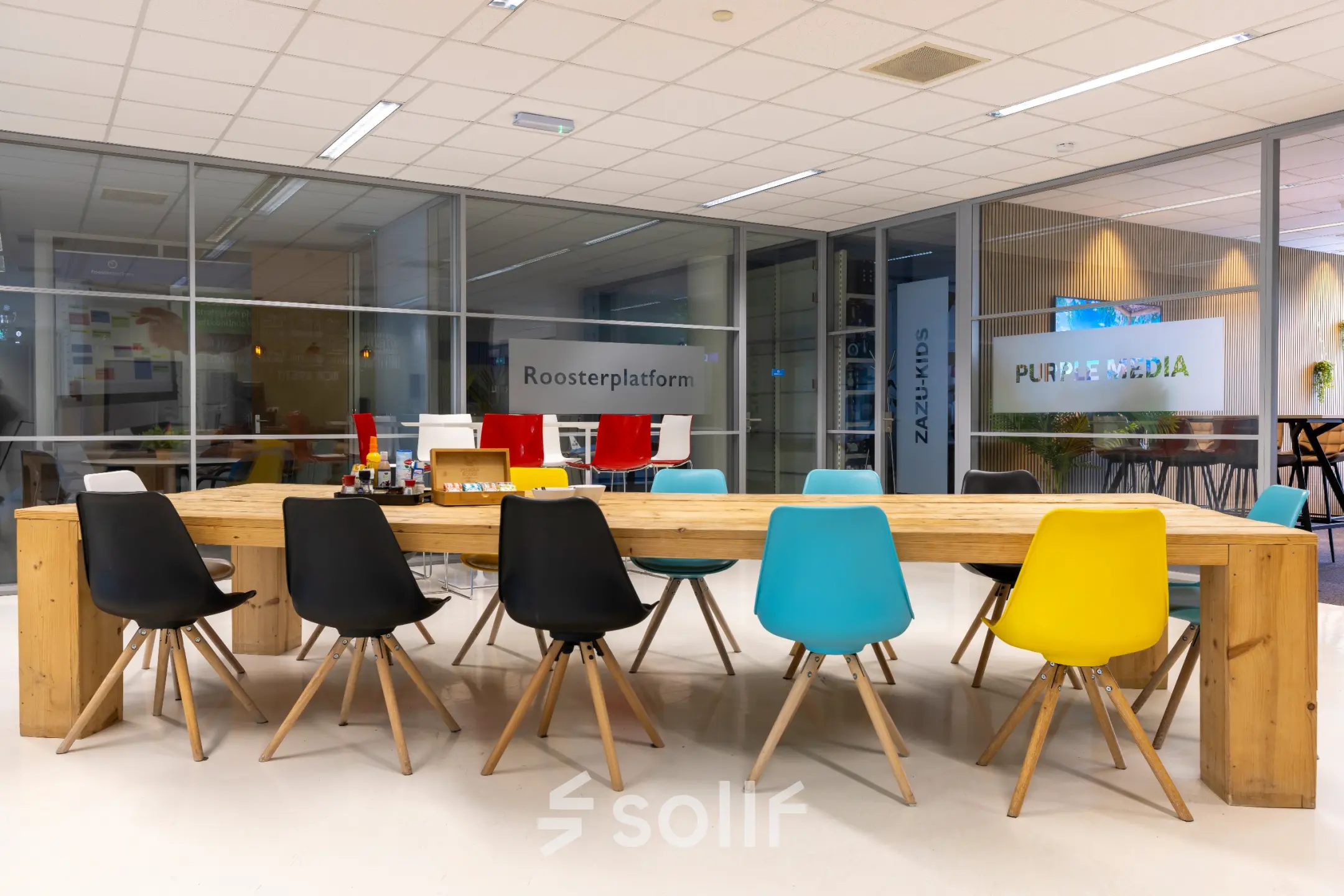 Spacious and colorful office space at Amalialaan 126, Baarn, perfect for rent office space, featuring vibrant chairs around a wooden table amidst a modern glass interior.