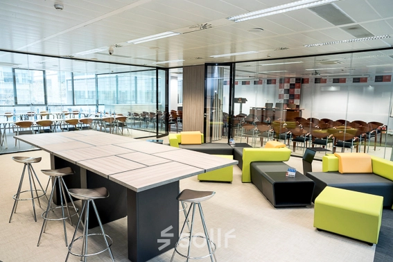 A modern office space at Carrer de Llull 321, Barcelona, featuring sleek tables, vibrant seating, and large glass partitions, ideal for meetings or casual gatherings. Perfect for office space rental.