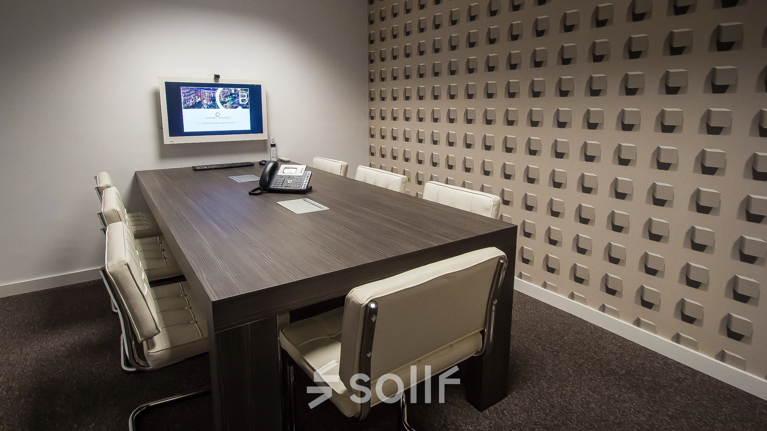 A furnished meeting room with a wooden table, chairs, and a wall-mounted screen at an office space rental on Carrer d'Aribau 161 in Barcelona Eixample.