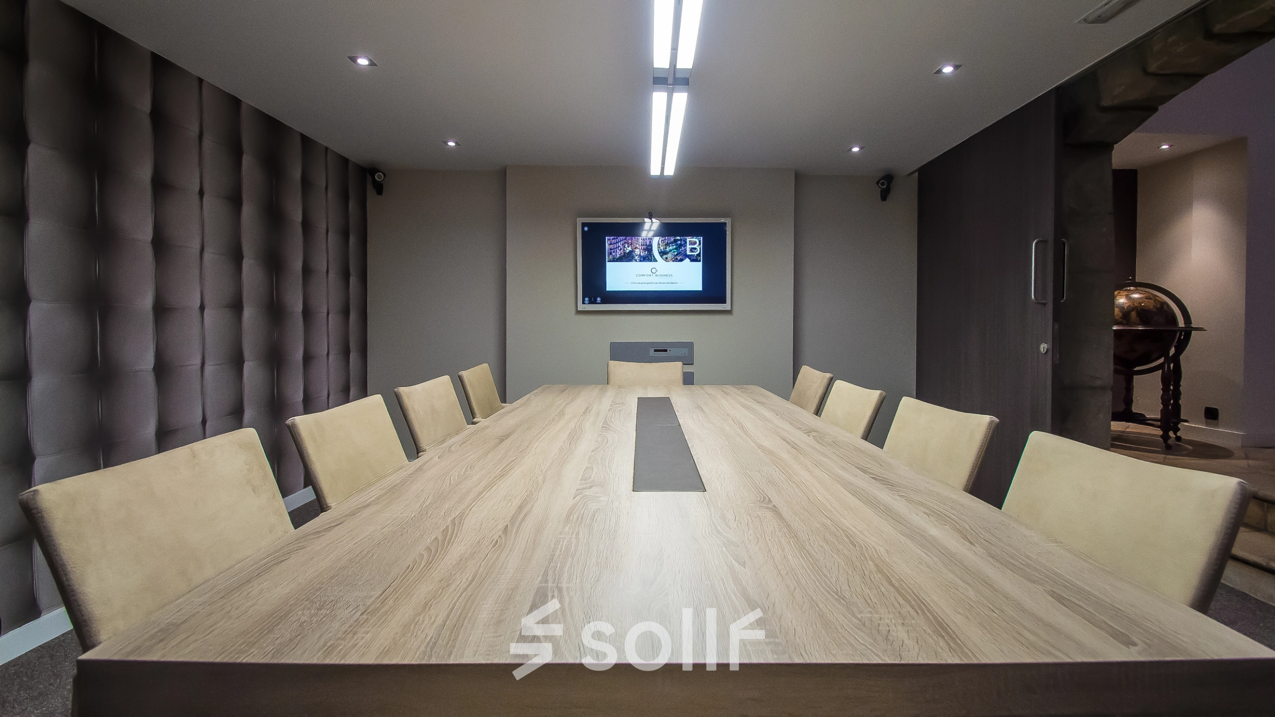 Modern conference room at Carrer d'Aribau 161, Barcelona Eixample with a large wooden table, cushioned chairs, and a wall-mounted screen, ideal for office space rental.