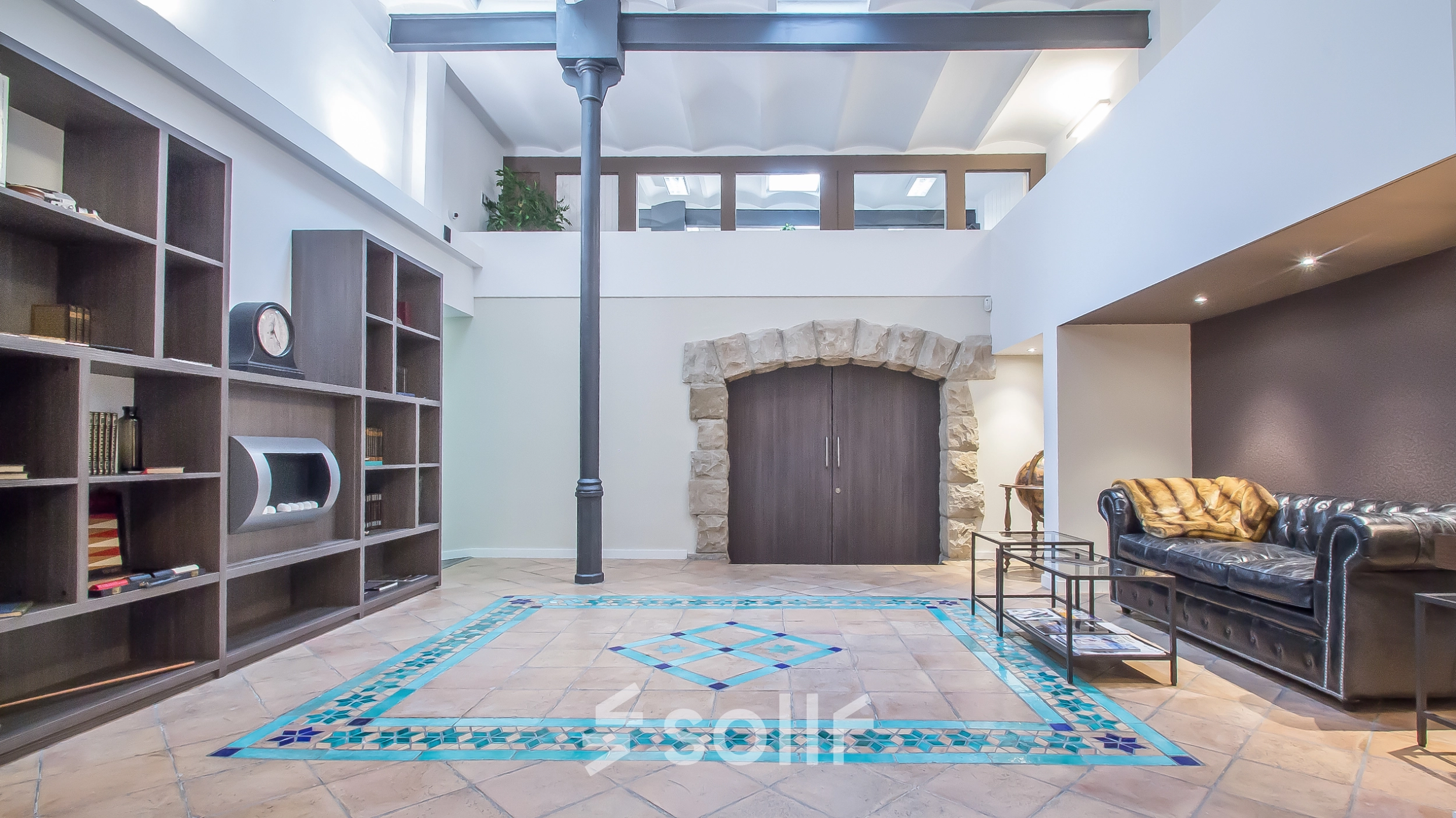 Spacious office space for rent in Barcelona Eixample, featuring stylish tiled flooring, a comfortable seating area, and large bookcases. Ideal for office space rental at Carrer d'Aribau 161.