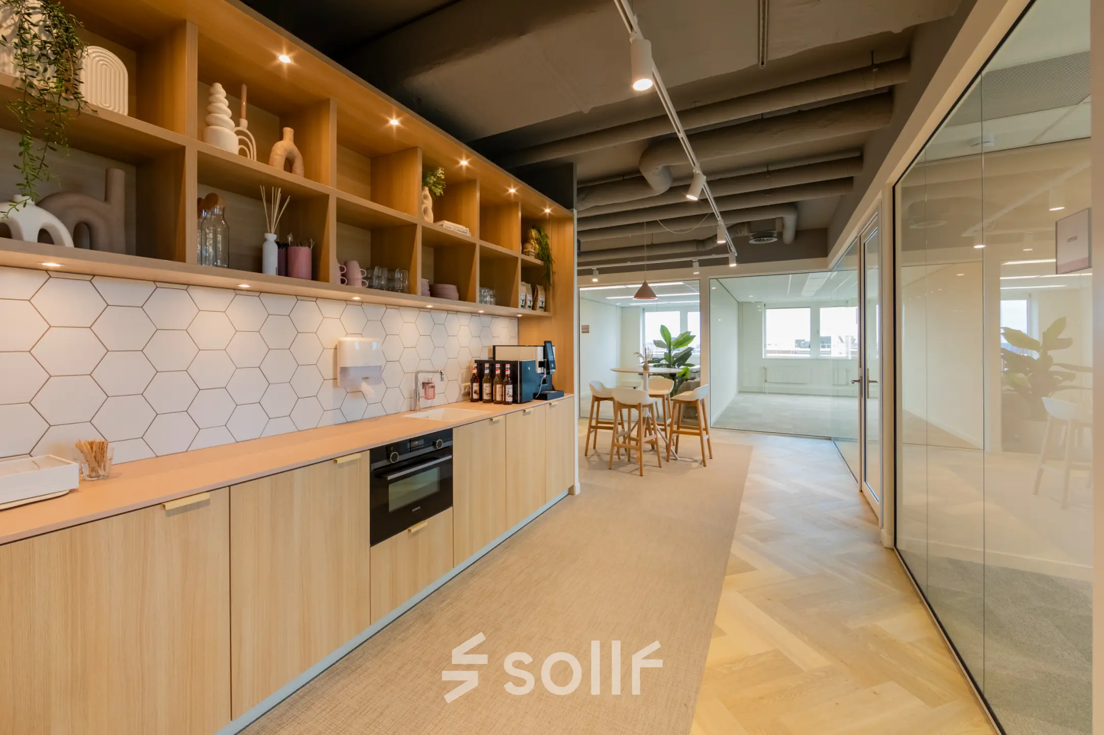 Modern office space at Baron van Nagellstraat 136, Barneveld, featuring a stylish pantry area with sleek wooden cabinets and decorative shelves, available for rent. Glass walls lead to a bright, inviting workspace.
