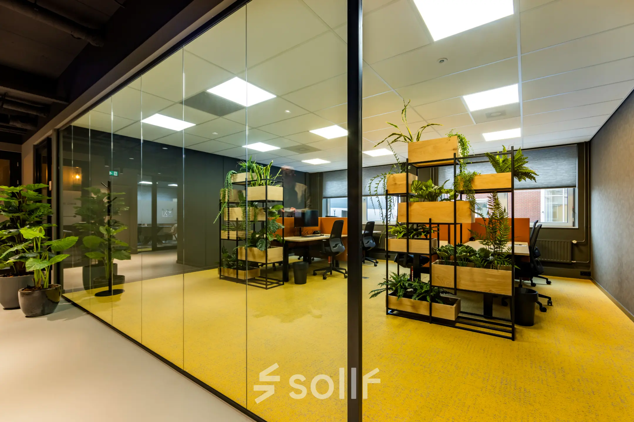 Bright office space with glass walls, modern furniture, and abundant plants at Baron van Nagellstraat 136, Barneveld. Ideal for office space rental with a vibrant and open-floorplan atmosphere.