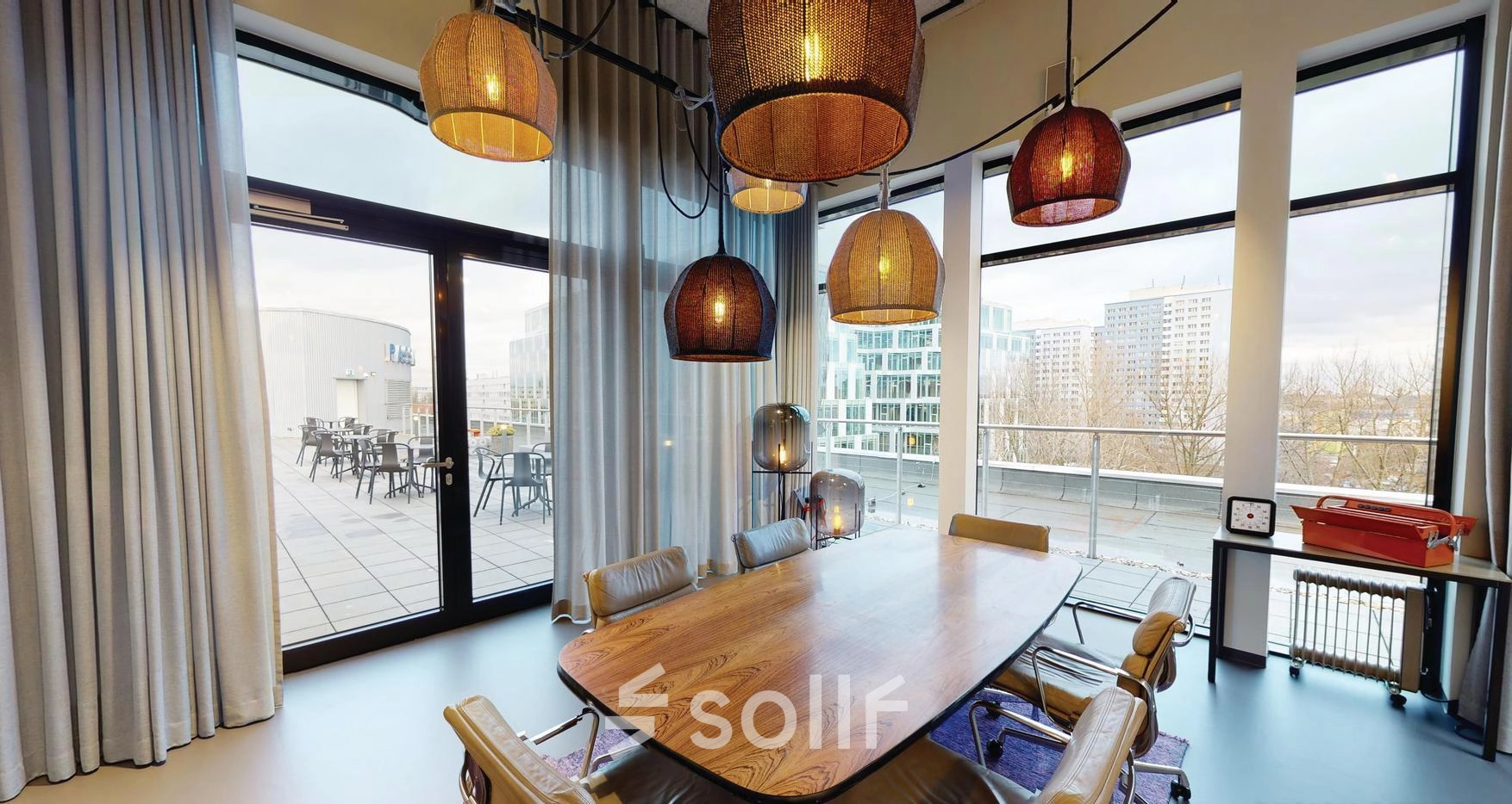 Spacious office space rental in Berlin Friedrichshain with a large conference table, stylish chairs, and modern lighting. Windows open to a scenic balcony view.