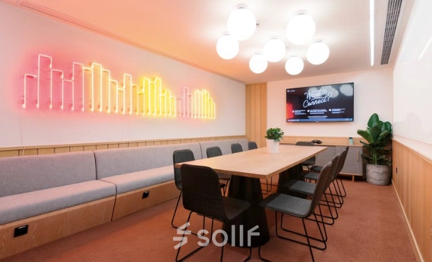 Conference room at Warschauer Platz 11-13, Berlin Friedrichshain, featuring a long wooden table surrounded by chairs, neon wall art, and a large screen. Ideal office space rental for meetings.