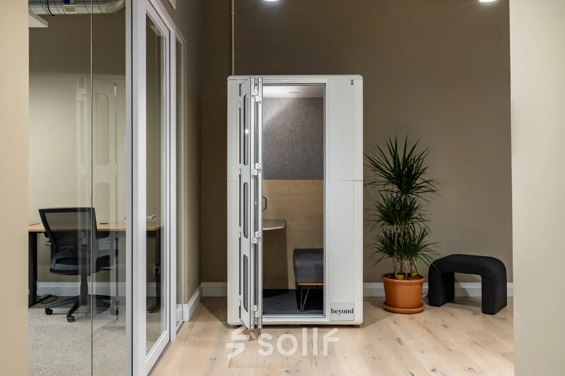 Modern office space with a private phone booth, rent office space at Chausseestraße 29, Berlin Kreuzberg. Features furnished work area and potted plant.