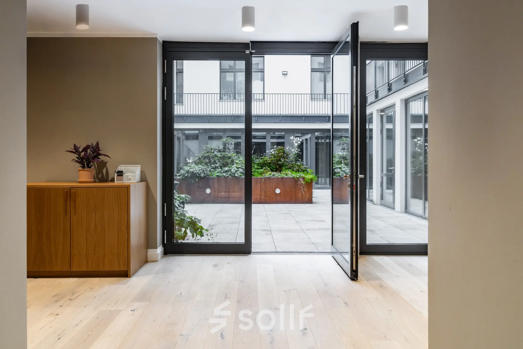 Office entrance with wooden flooring and glass doors leading to a courtyard, suitable for office space rental in Berlin Kreuzberg.
