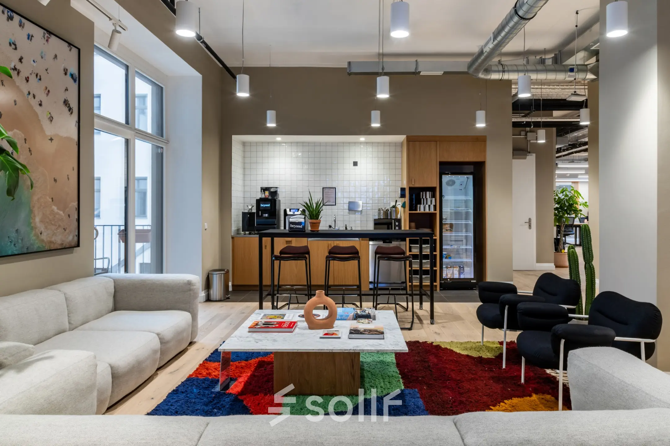 Spacious Berlin Kreuzberg office to rent with a stylish lounge area, featuring cozy armchairs, a vibrant rug, and a modern kitchen space.