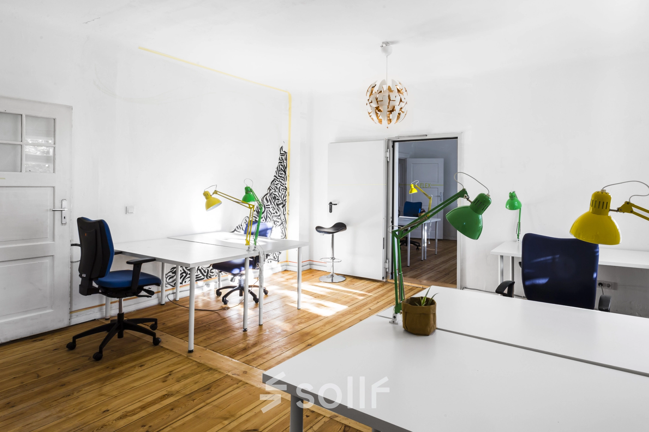 Bright office space at Blockdammweg 1, Berlin Lichtenberg, featuring wooden floors, white desks, colorful lamps, and modern decor, ideal for office space rental.