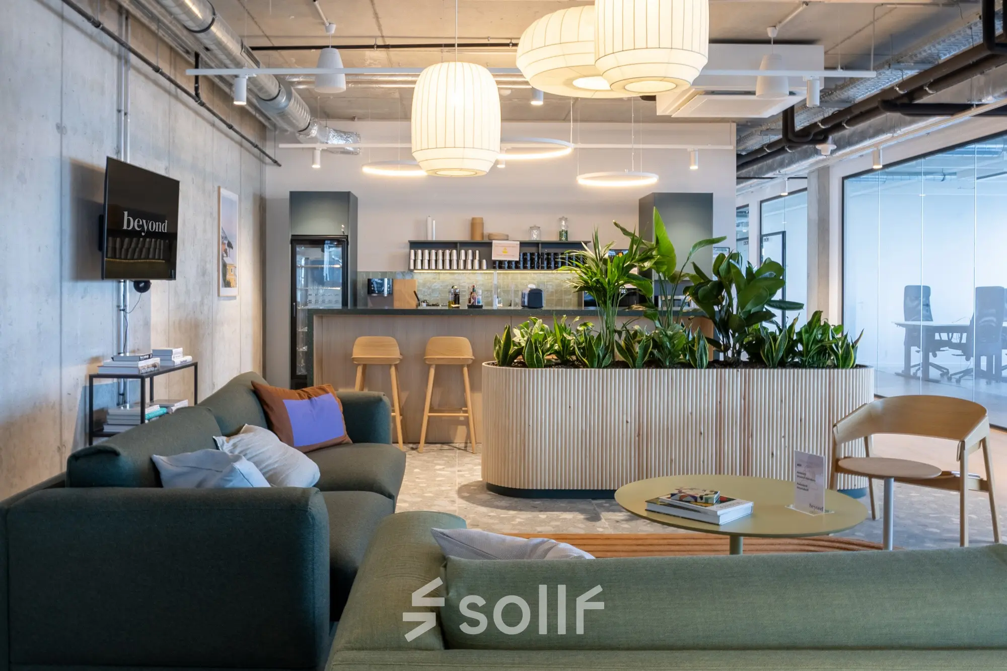 Modern office lounge area at Heidestraße 34 in Berlin Mitte with comfortable seating, a bar counter, and lush plants for rent office space enjoyment.