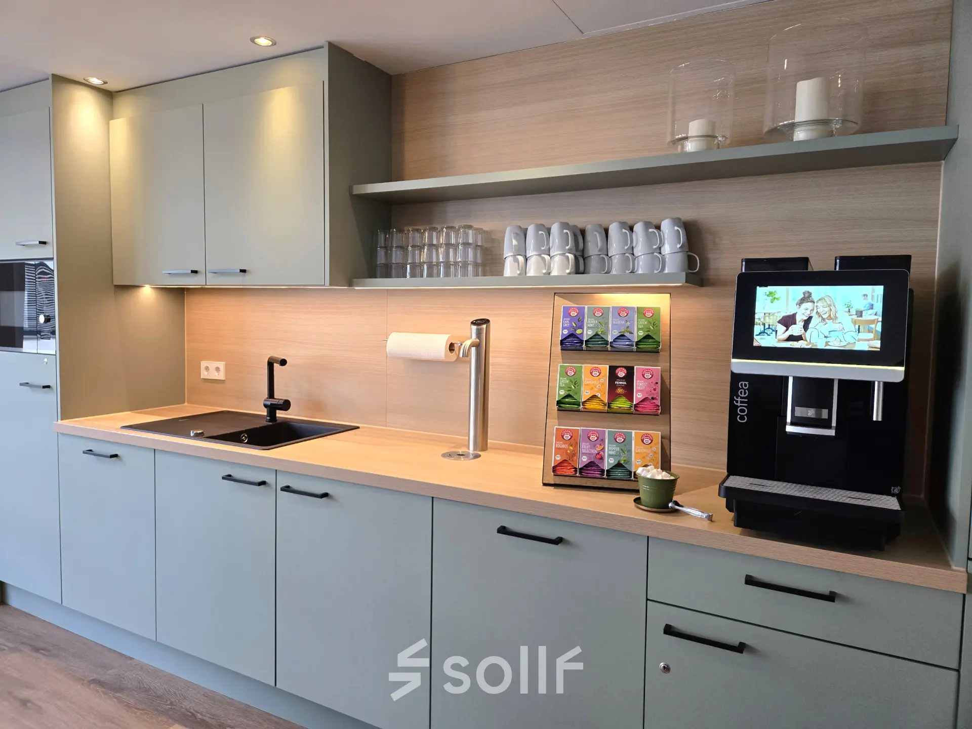 Compact kitchenette in an office space, equipped with cabinets, a sink, a coffee machine, and neatly arranged cups and teabags on display at Leipziger Platz 15, Berlin Mitte.