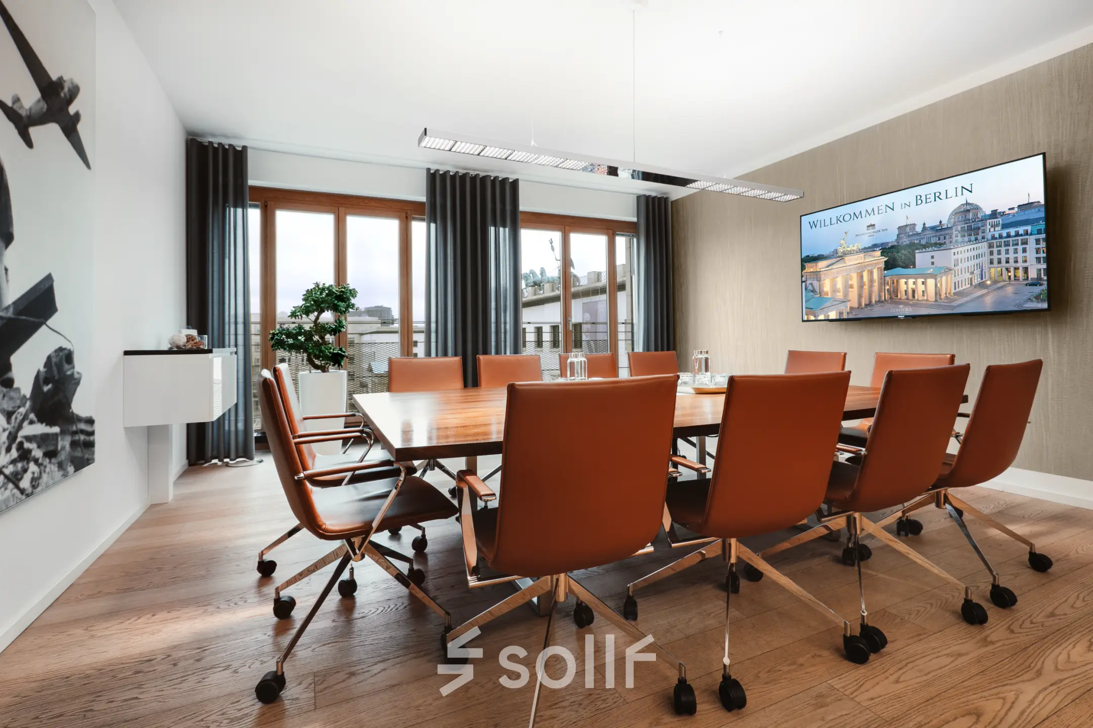 Conference room with a large wooden table, stylish leather chairs, and a decorative plant by the window at Pariser Platz 6a, perfect for office space rental.