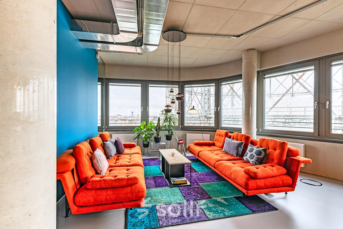 Bright office lounge with orange couches and colorful rugs, located at EUREF-Campus 22, Berlin Schöneberg, ideal for office space rental.