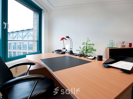 A furnished office space at Flughafenallee 26, Bremen Neustadt, featuring a desk with office supplies, a chair, and a large window offering natural light. Ideal for office space rental.