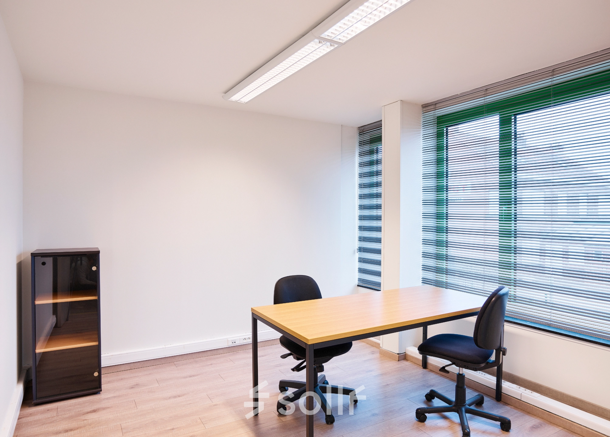 Bright office space with a wooden desk and chairs by large windows in Leuvensesteenweg 613, ideal for rent. Natural light enhances the office space rental.