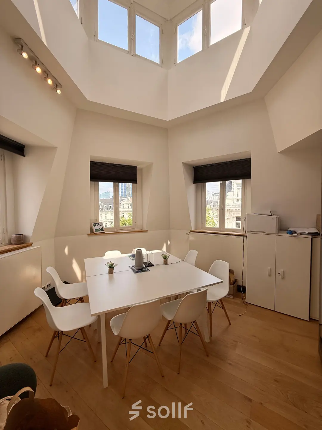 Bright office space with a central table and chairs under a skylight, ideal for office space rental in Brussels Center.