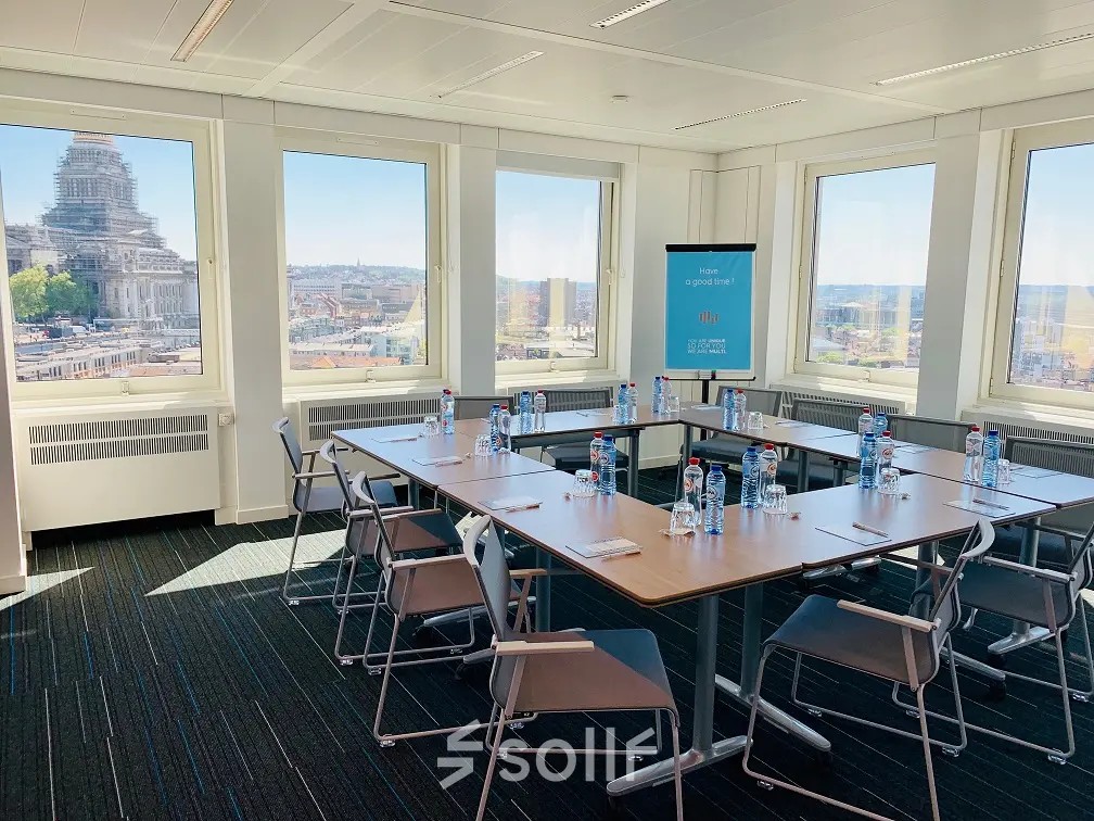 Bright conference room at Rue Joseph Stevens 7 in Brussels Center, ideal for office space rental, featuring large windows with city views, a U-shaped table setup, and multiple chairs.