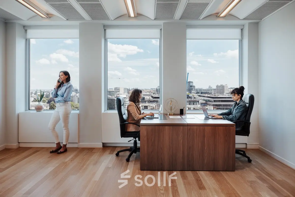 Spacious office to rent in Brussels European District with two employees working at desks and one person on the phone by the window.