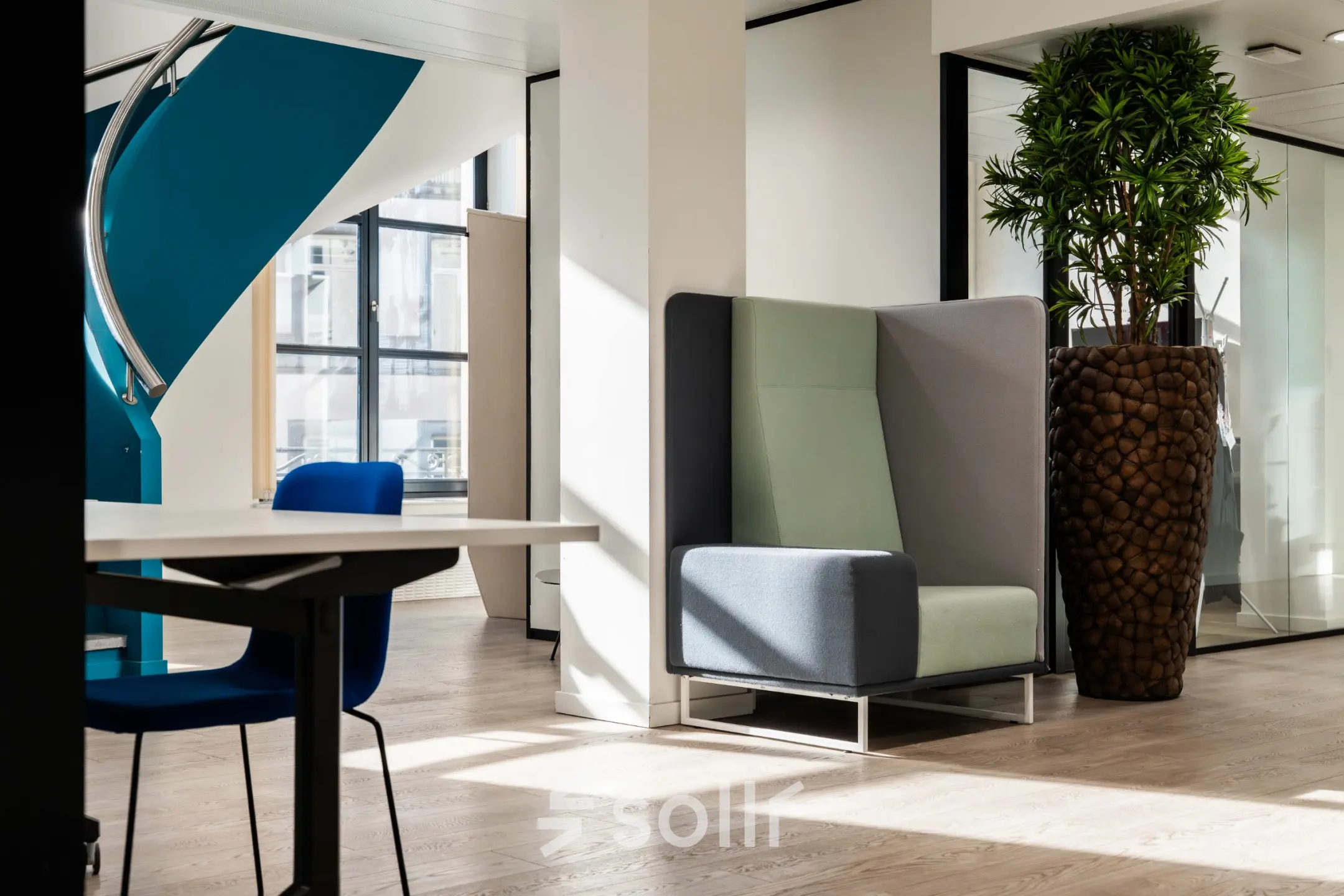 Modern office space with bright natural light in Rue des Colonies 56, Brussels European District, ideal for office space rental. Features include sleek furniture, stylish seating, large windows, and a touch of greenery.