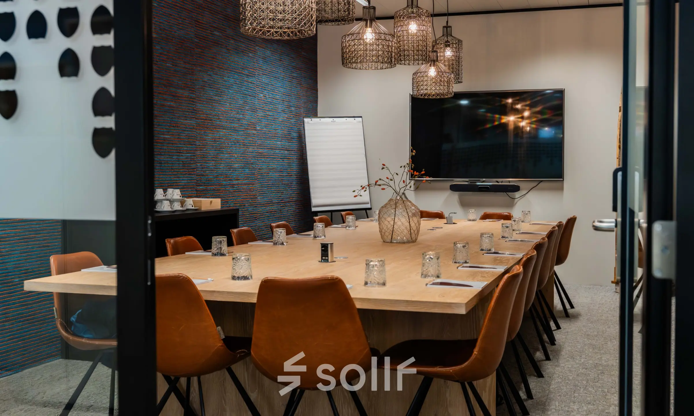 Furnished meeting room in a Brussels office available for rent, featuring a long table, chairs, and a wall-mounted TV.