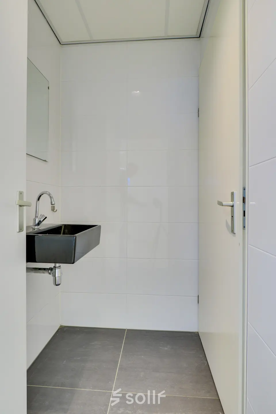 Minimalistic restroom with a sleek black sink and white tiled walls at Regulierenring 2, ideal for office space rental.