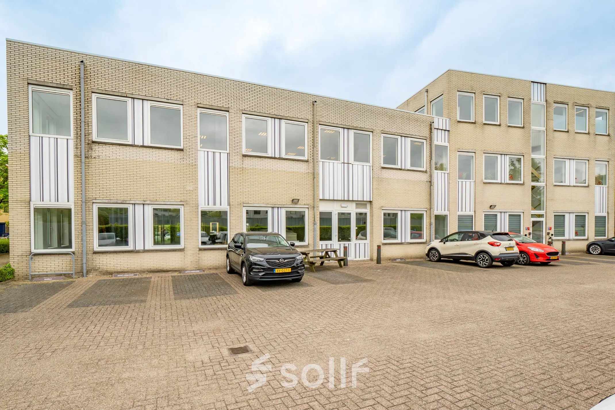 Exterior view of an office building at Regulierenring 2, Bunnik, featuring a parking area with several cars.