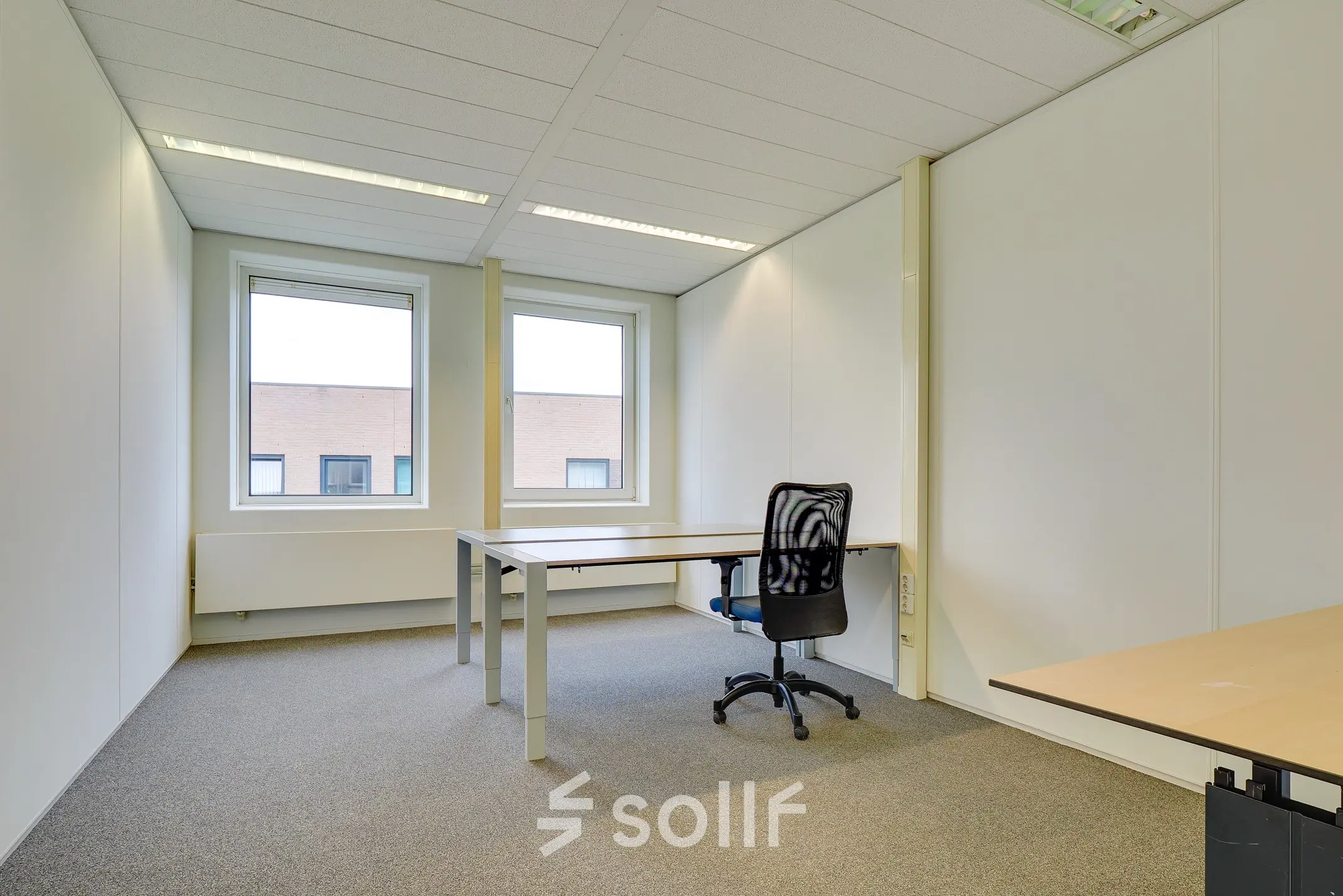 Bright office space with large windows available for rent at Regulierenring 2, Bunnik. Minimalist design, ready for office space rental with basic furniture setup including desks and chairs.