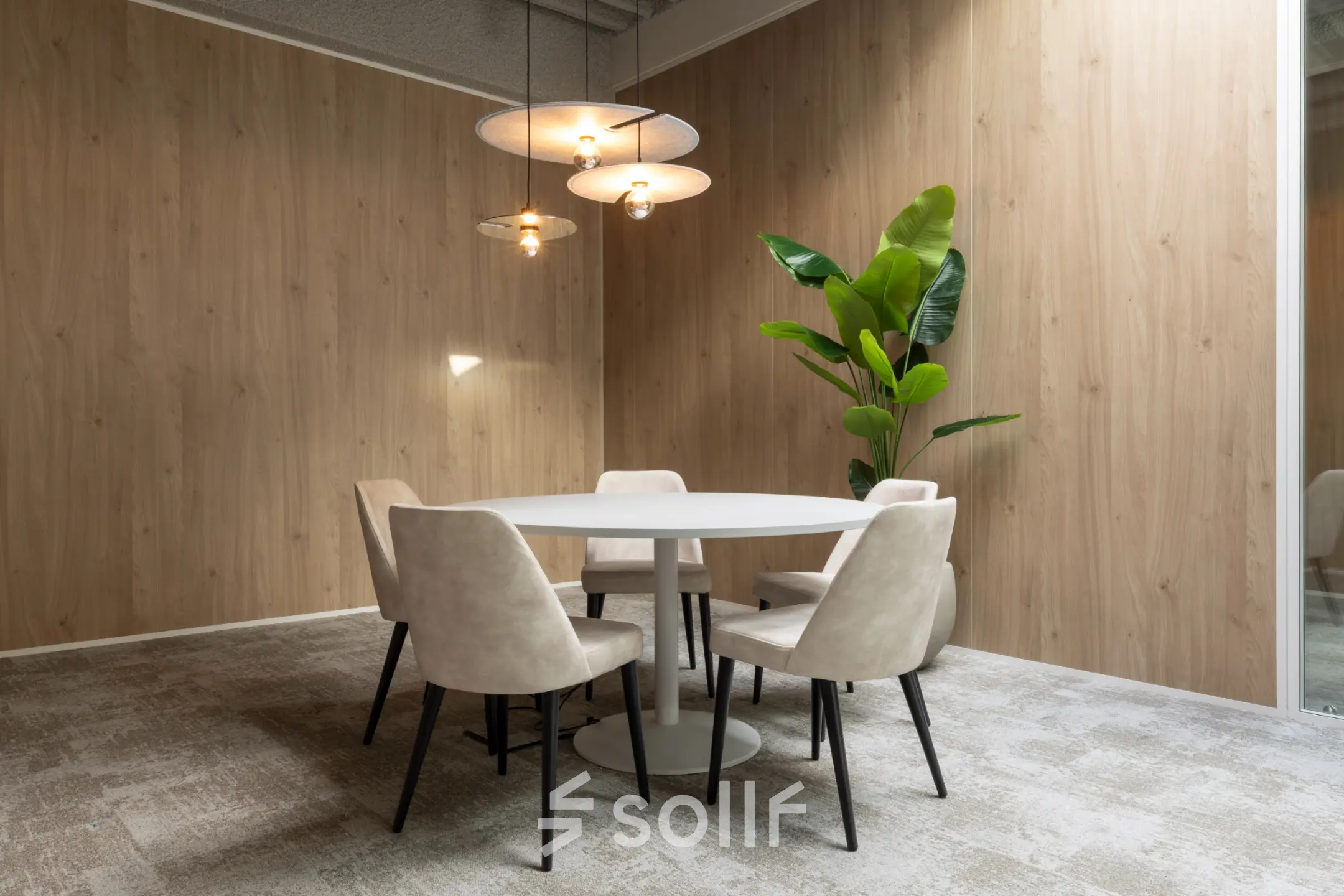 Cozy office space rental with round table, chairs, modern lighting, and a plant in a wood-paneled room at Essebaan 63.