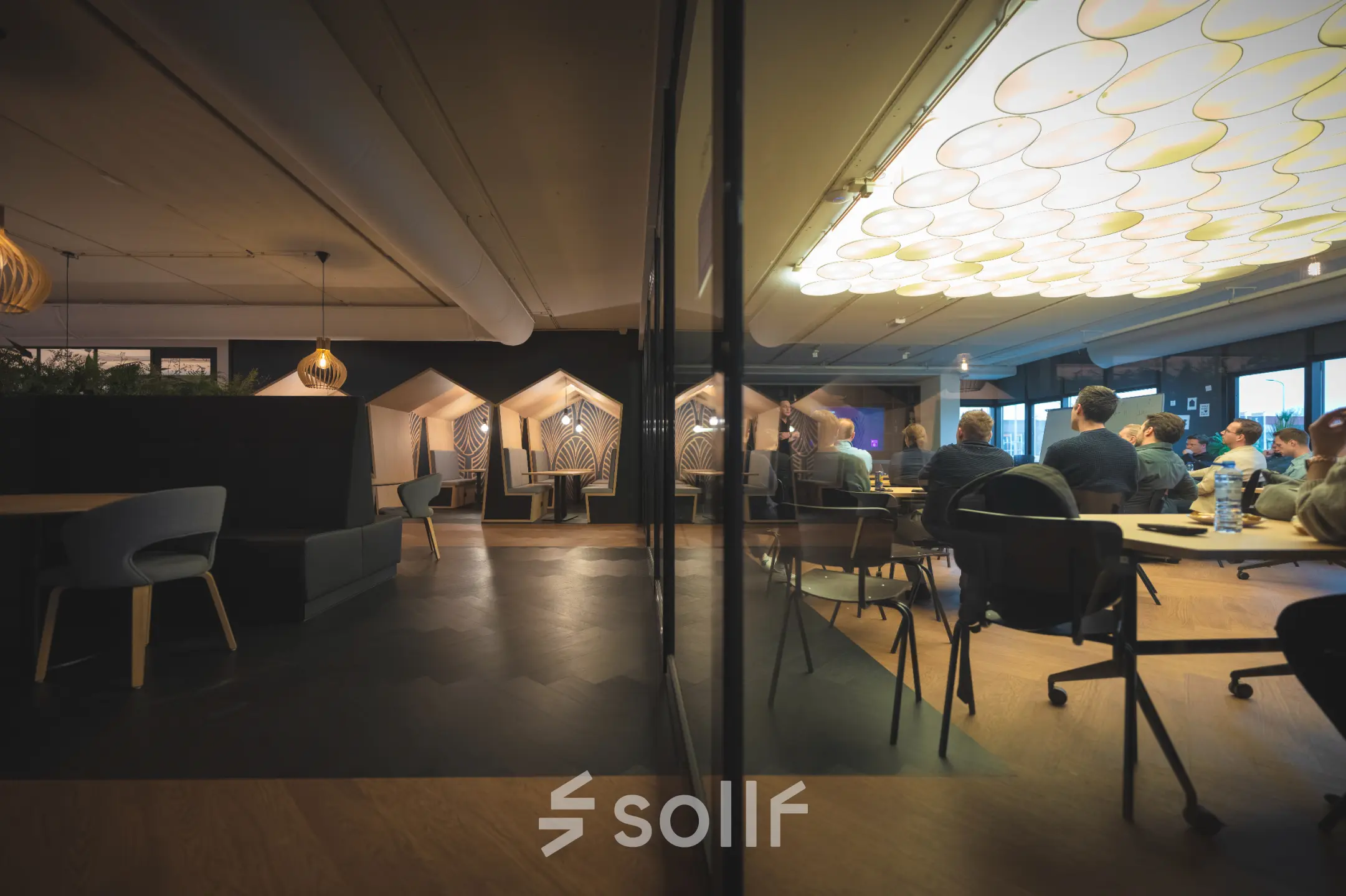 Office space rental in Capelle aan den IJssel at Rietbaan 2-12, featuring modern lighting, seating areas, and people engaged in business discussions next to stylish decor.