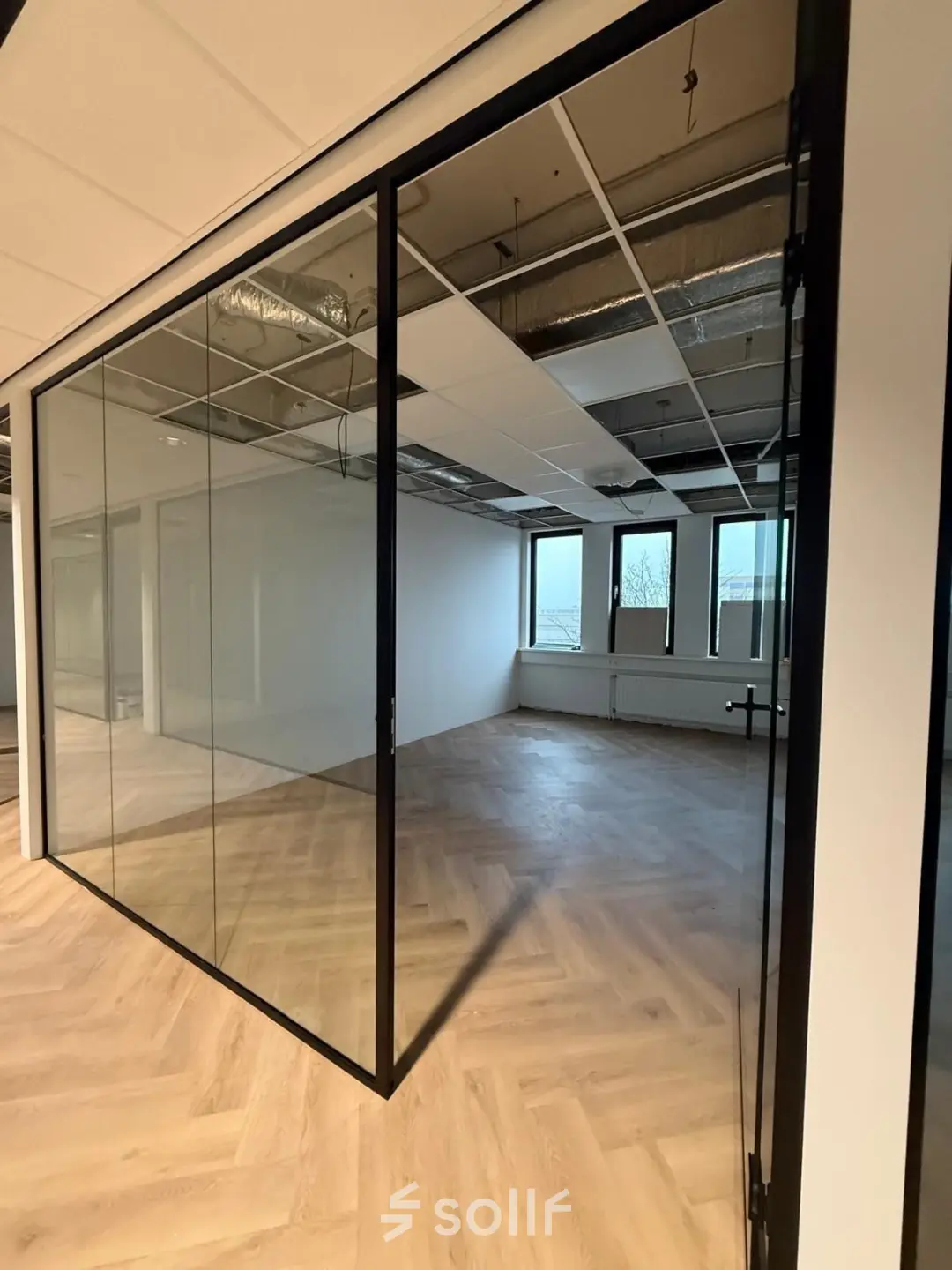 A modern office space rental at Vlierbaan 20, Capelle aan den IJssel, featuring glass walls, herringbone floors, and large windows for natural light.