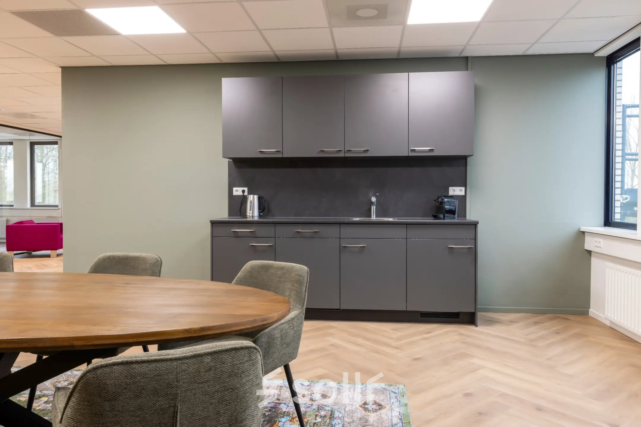 Modern furnished office space for rent at Vlierbaan 20 with a kitchenette featuring dark cabinets and a round table with chairs.