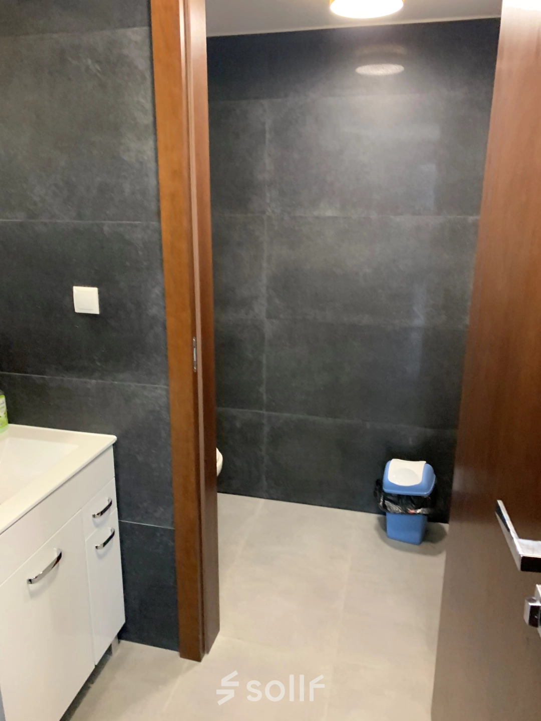 Modern office restroom with dark tiles, sink cabinet, and waste bin at Jastrzębia 24 in Cracow Podgorze Duchackie, ideal for office space rental needs.