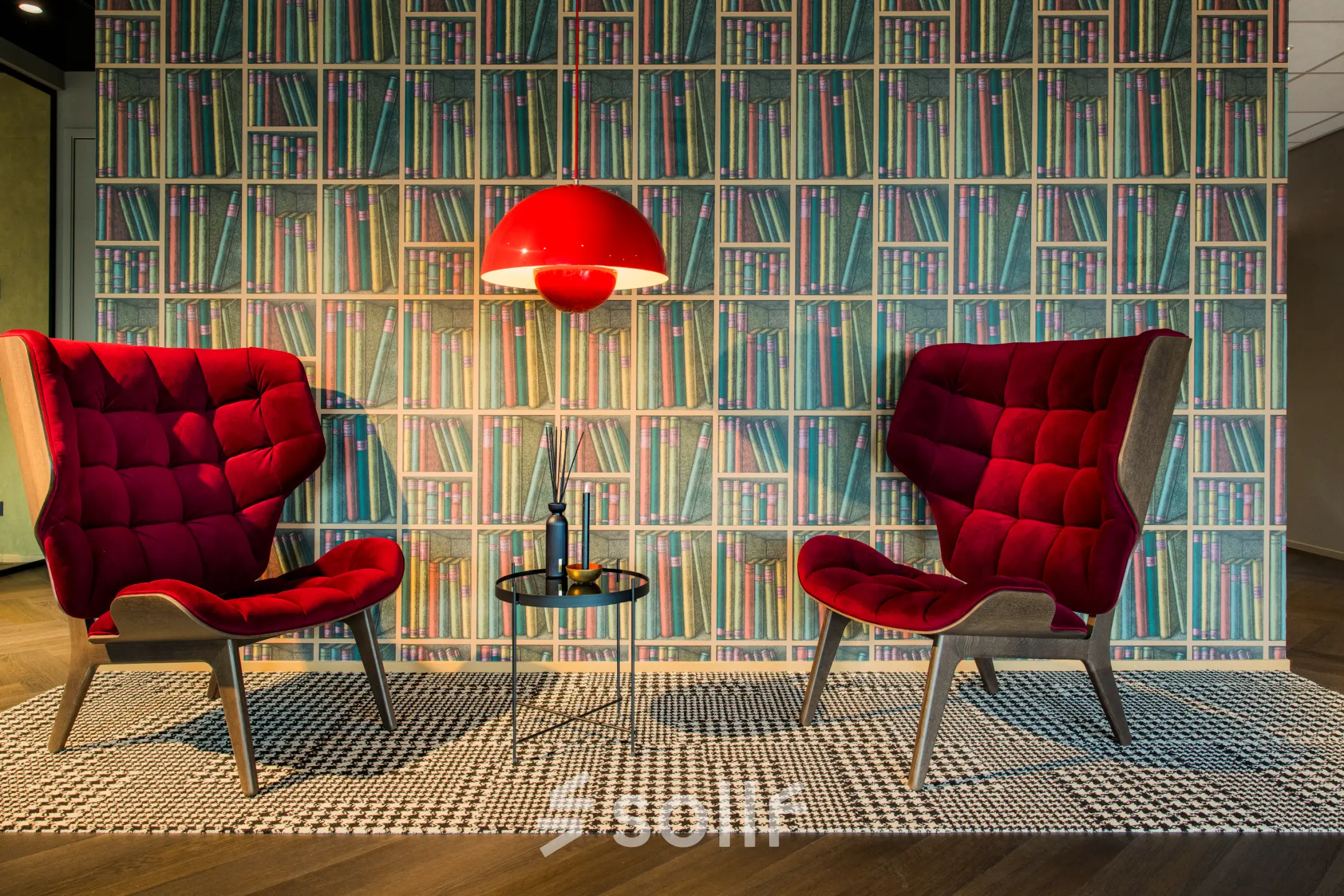Furnished lounge area at Rijnzathe 12, De Meern with two red chairs and a book-patterned wall, ideal for renting office space and relaxed meetings.
