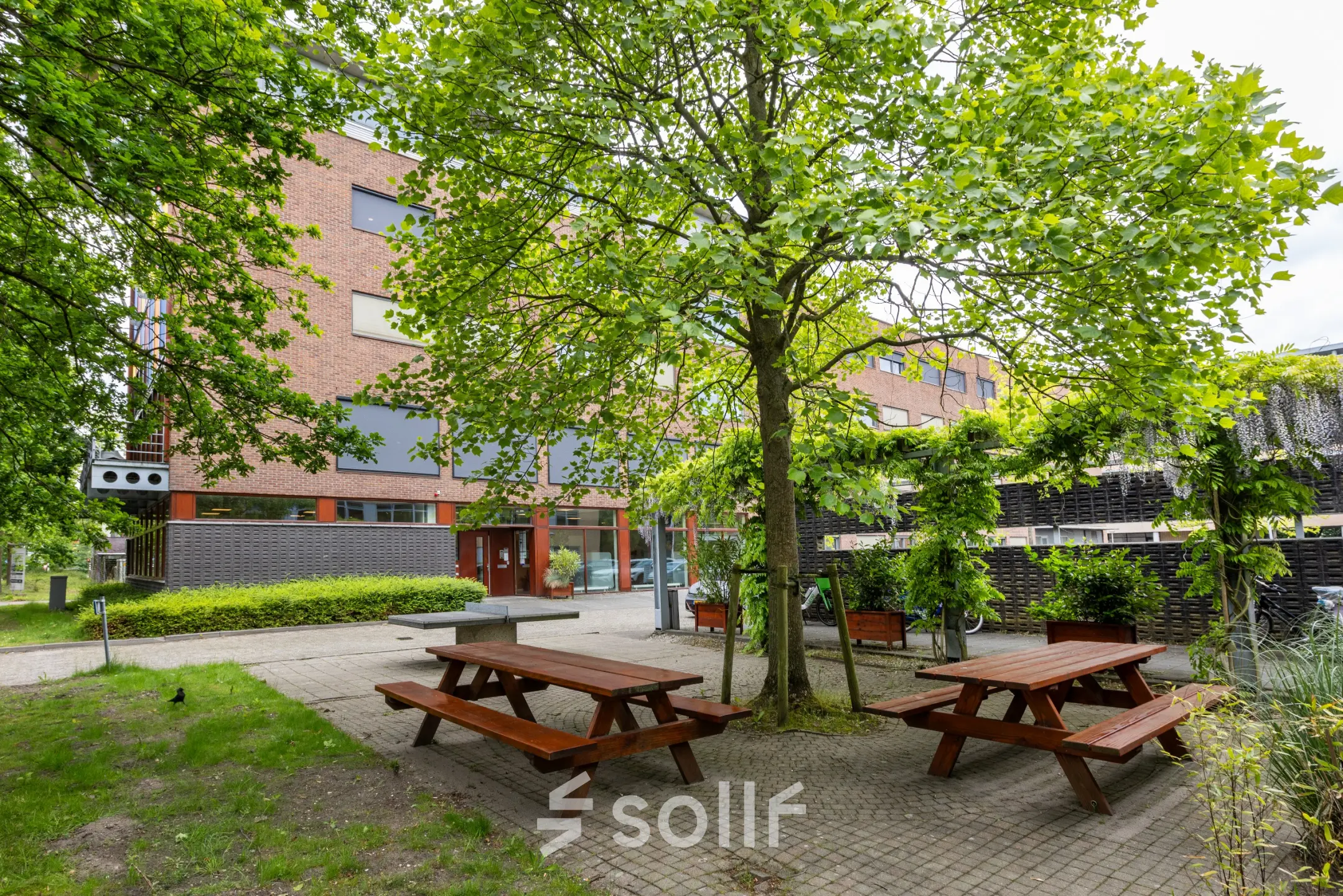 Exterior view of an office building at Delftechpark 9, Delft, featuring a green outdoor seating area ideal for office space rental breaks.
