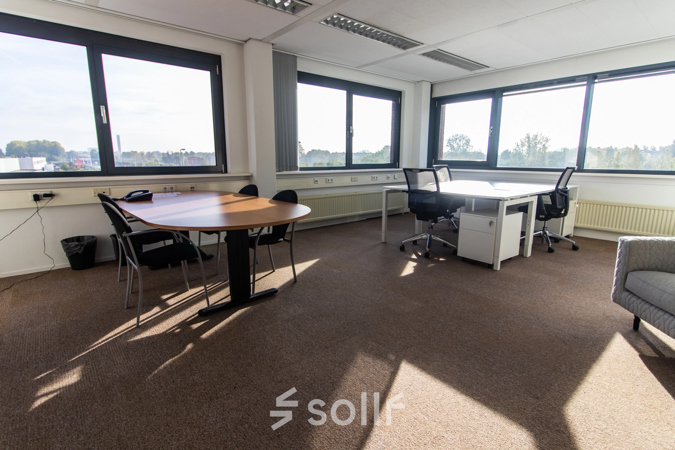 Bright office space for rent at Marshalllaan 2, Delft, featuring large windows, desks, and chairs suitable for a productive work environment.