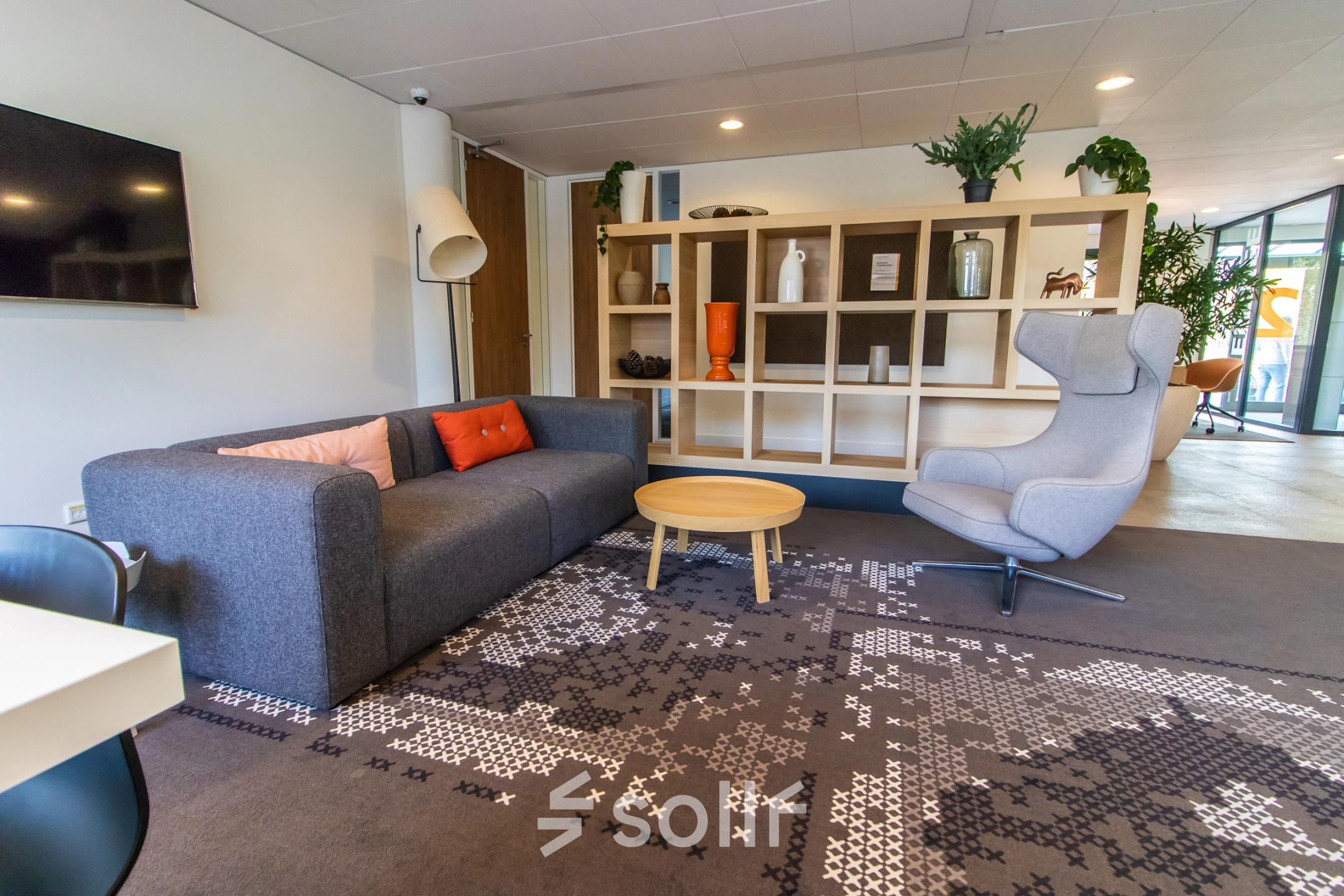 Cozy office space for rent at Marshalllaan 2, Delft, featuring a furnished lounge with a sofa, armchair, and decorative shelving. Ideal for office space rental.